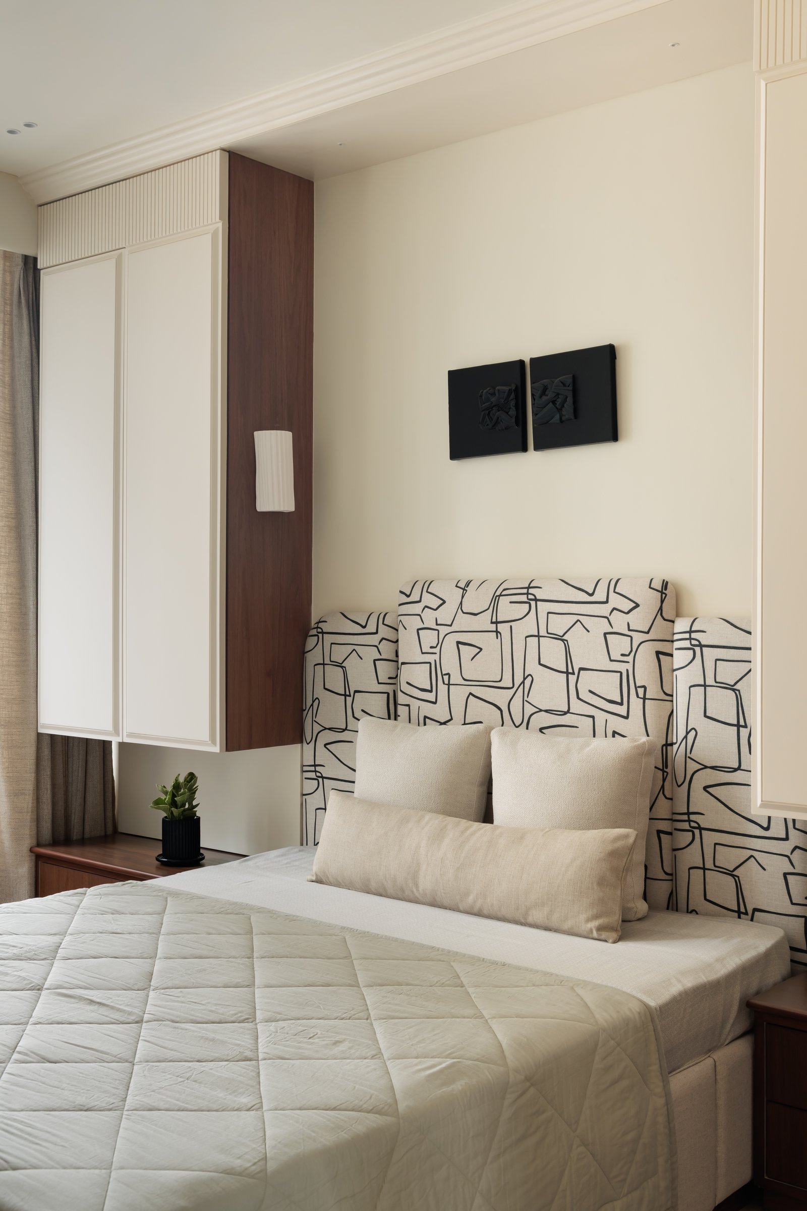 Another bedroom, where a graphic black-and-white printed headboard sits between panelled wardrobes and a slim walnut column