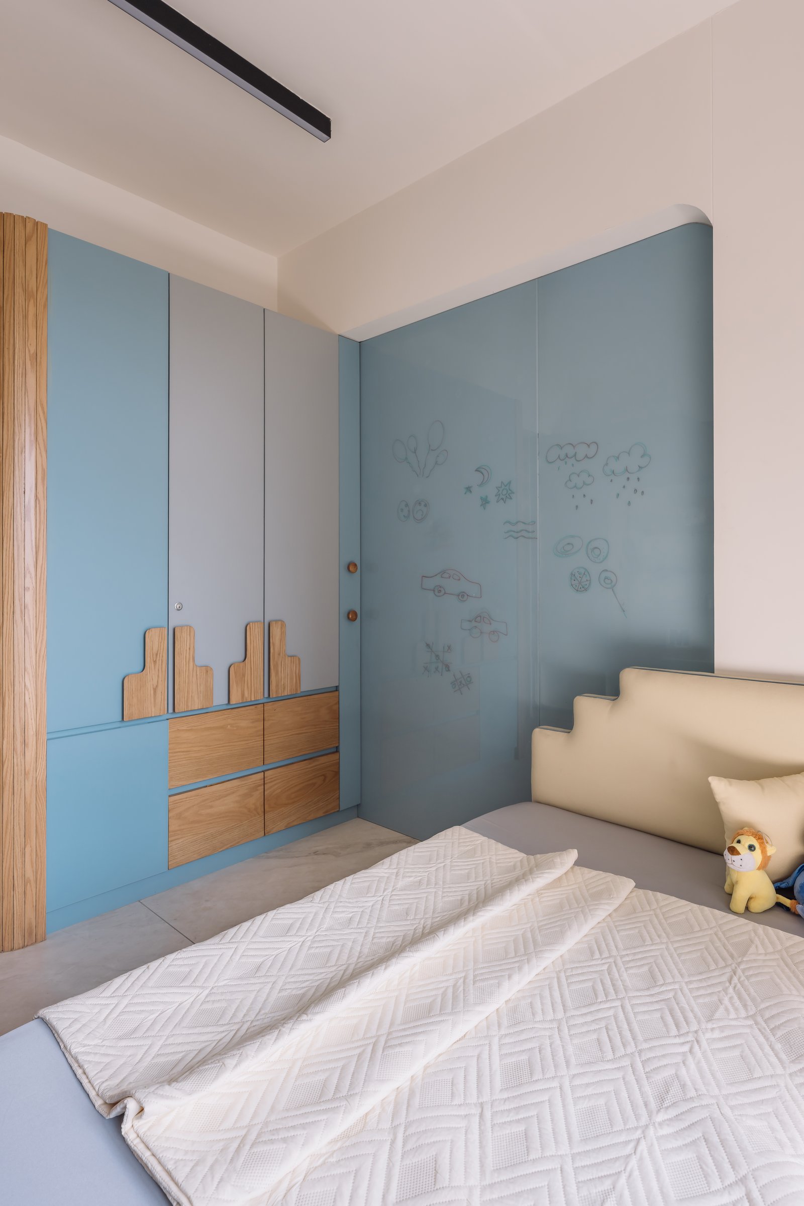 The children's room, where a muted blue palette and warm wood meet in a writable glass panel and a stepped headboard