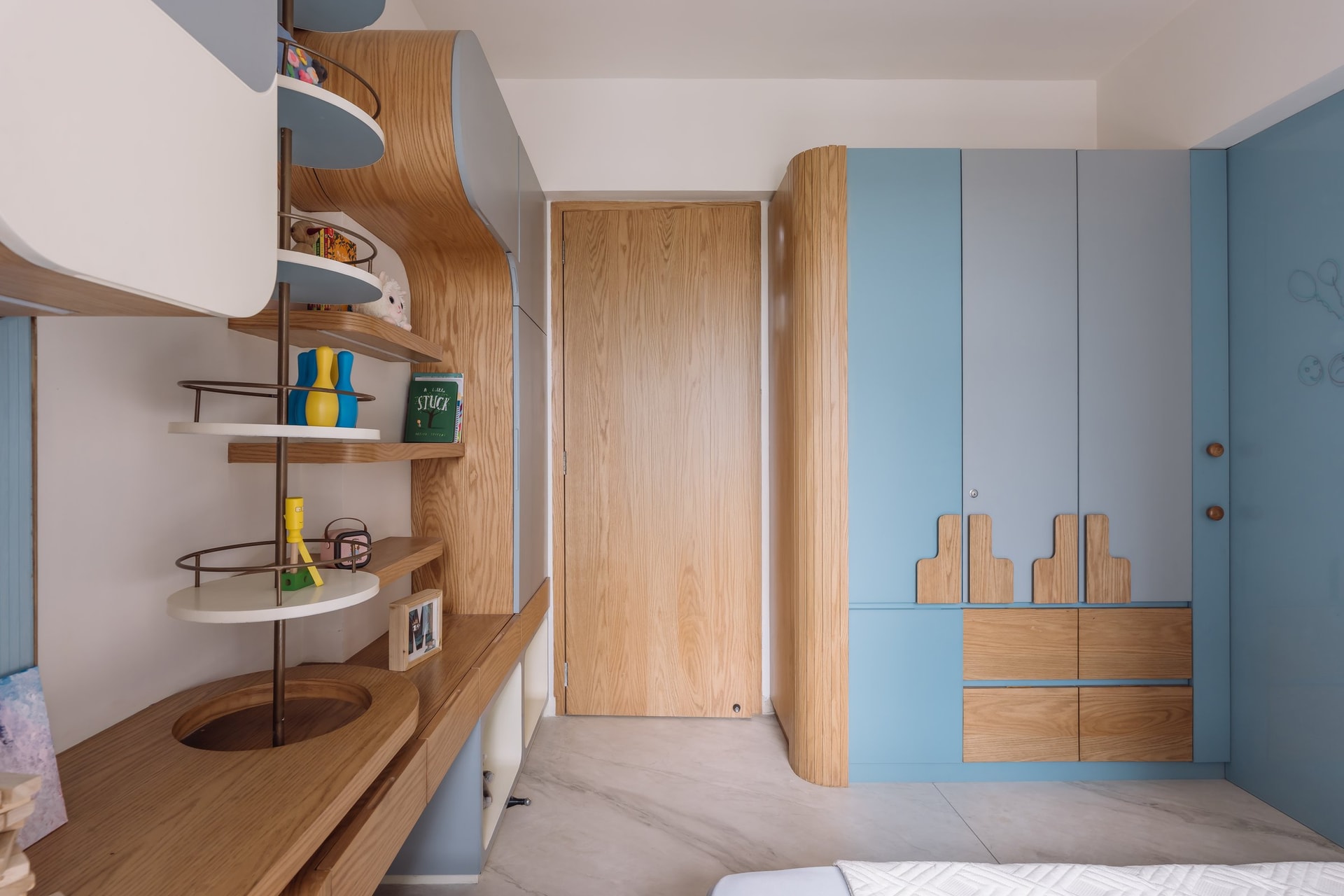 The children's room joinery, where shelving, desk and wardrobe read as a single integrated piece with a rotating column of circular shelves