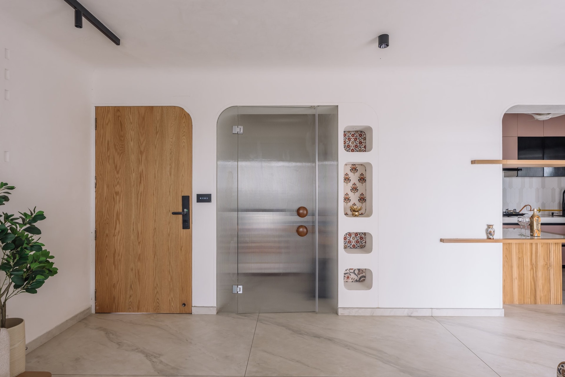 The entrance foyer, where a wooden door and reeded-glass partition sit beside a column of fabric-lined display niches, introducing the home's language of curves and openings