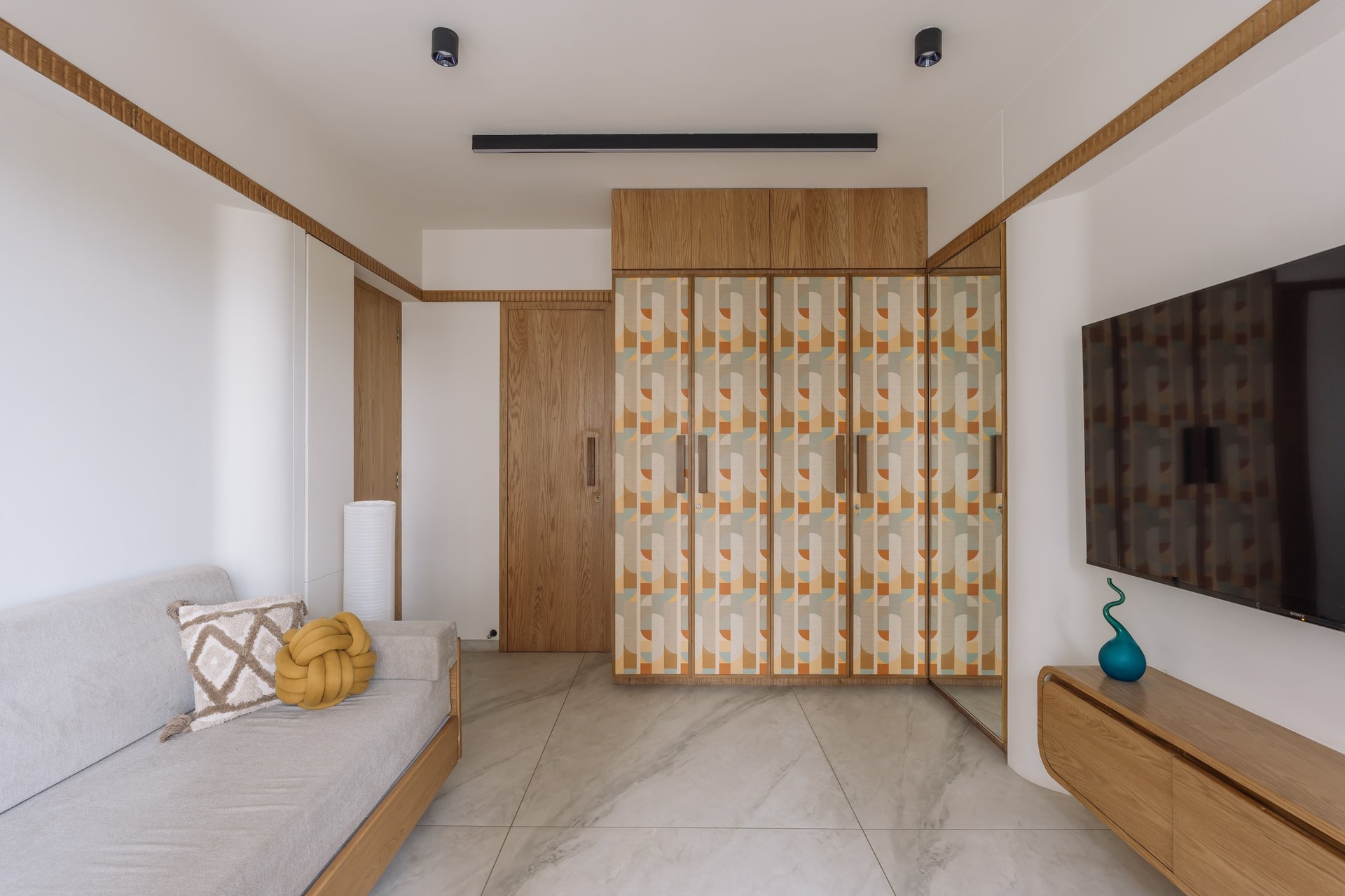 The second bedroom, where a graphic patterned wardrobe becomes the defining element, framed by a continuous reeded wooden band at picture-rail height