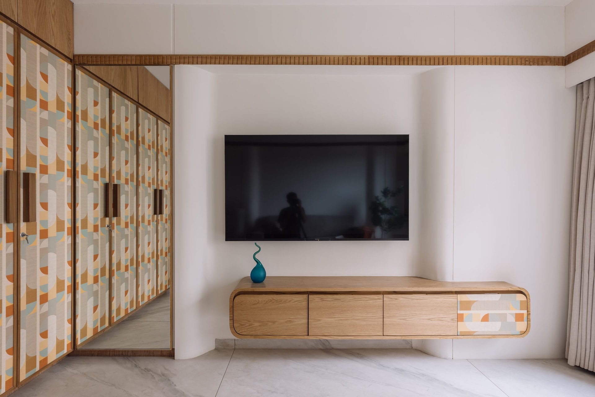 The media wall in the second bedroom, where a curved wooden console reinterprets the living room's box-form language at a smaller scale