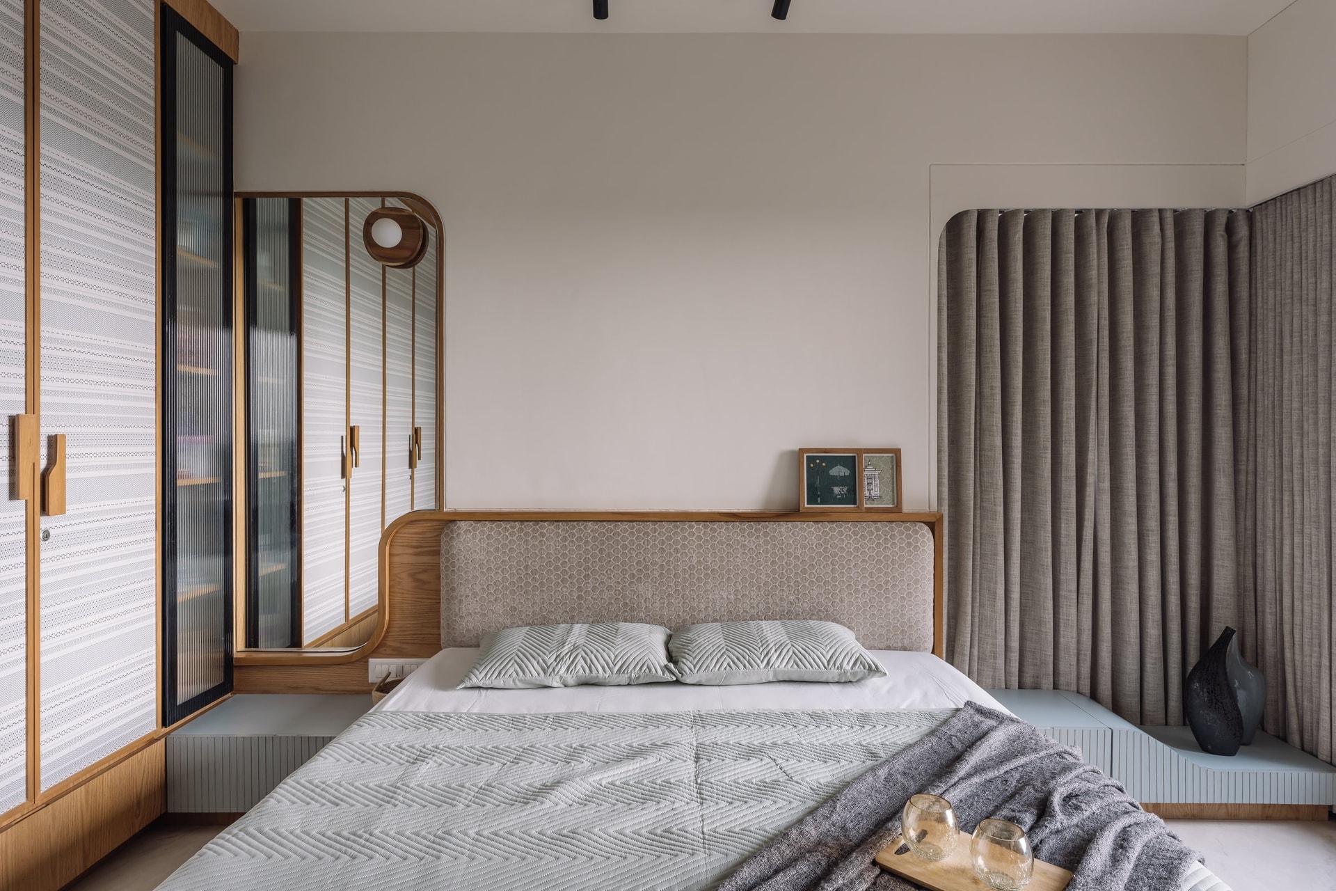 The primary bedroom, where an upholstered honeycomb-textured headboard is held within a curved wooden frame that extends into integrated bedside ledges