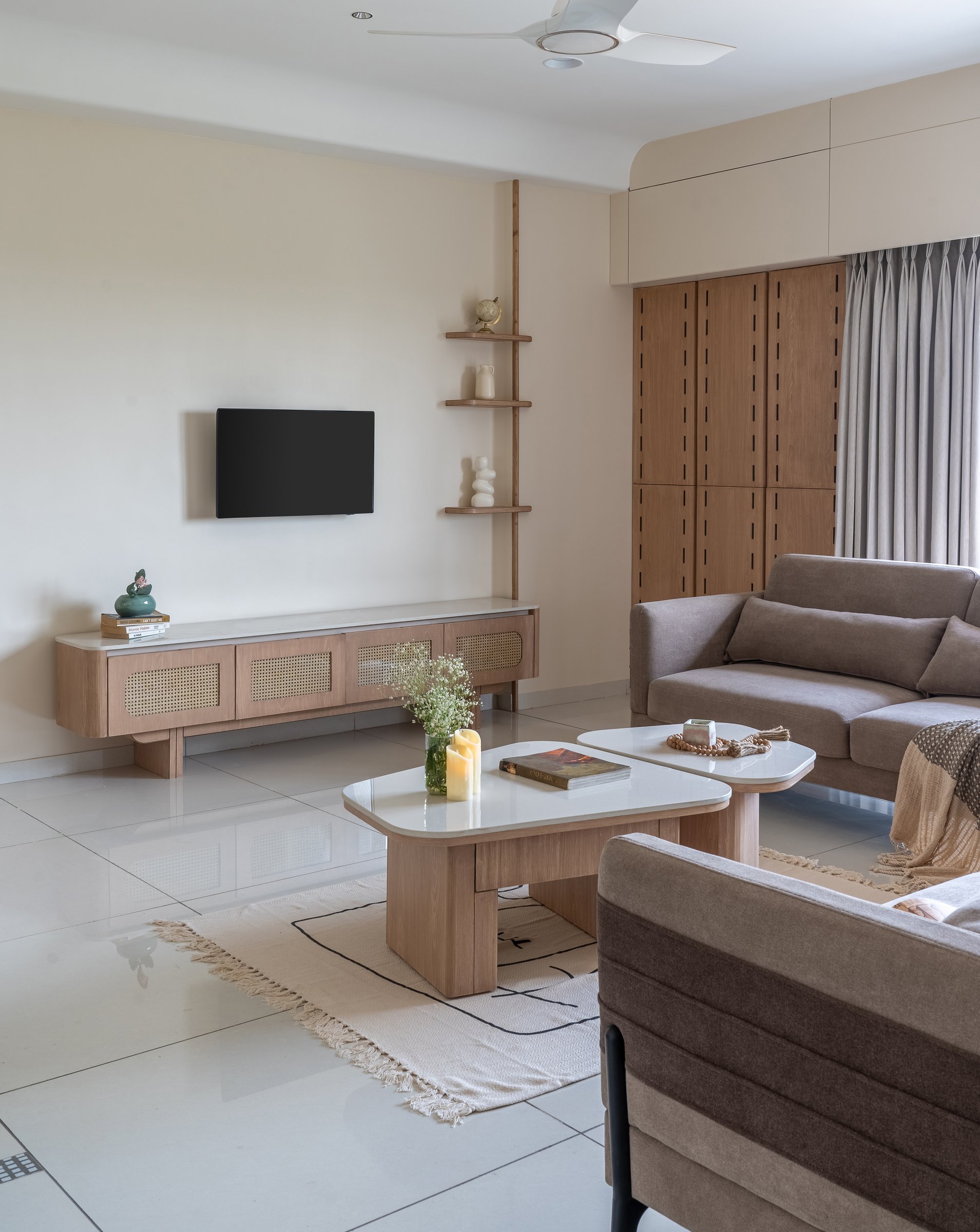 The media wall of woven cane fronts set within pale wooden joinery, with a slim vertical shelf climbing the corner