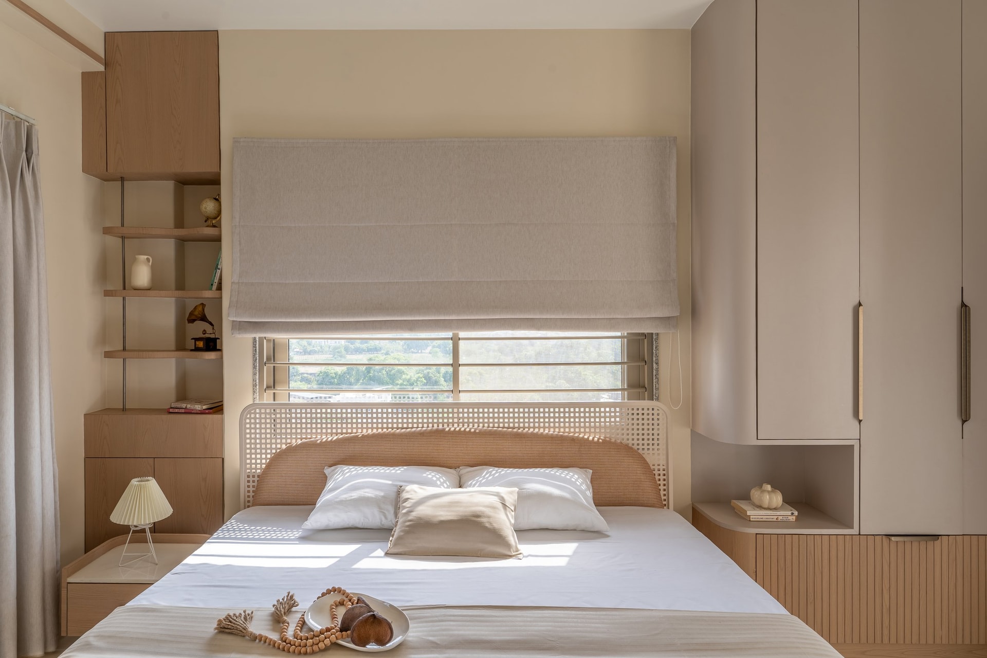 The master bedroom, with its curved cane headboard set against cream-plastered walls and flanked by warm wooden joinery