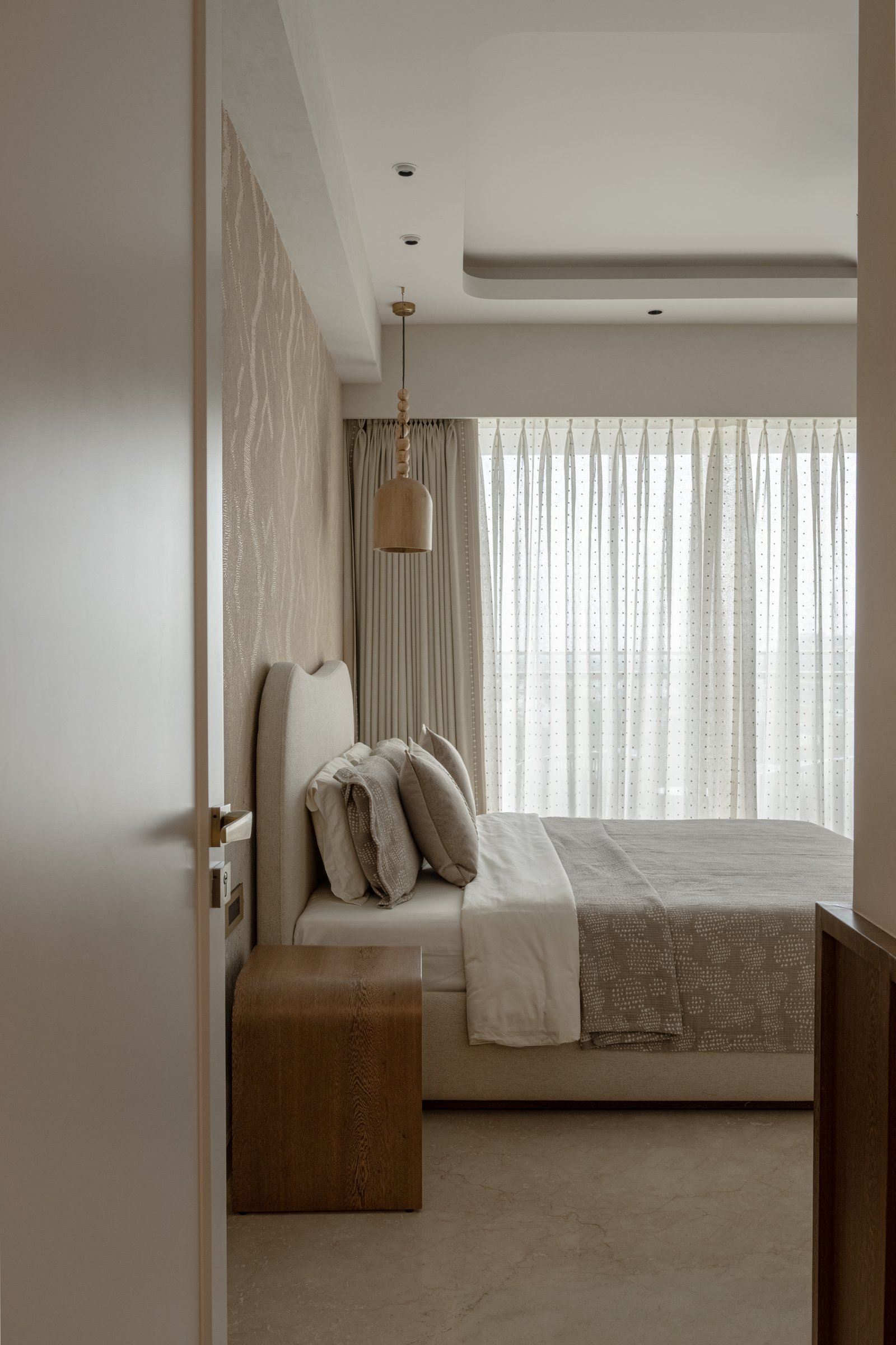 The second bedroom, with a tall upholstered headboard and a wooden pendant beside the bed