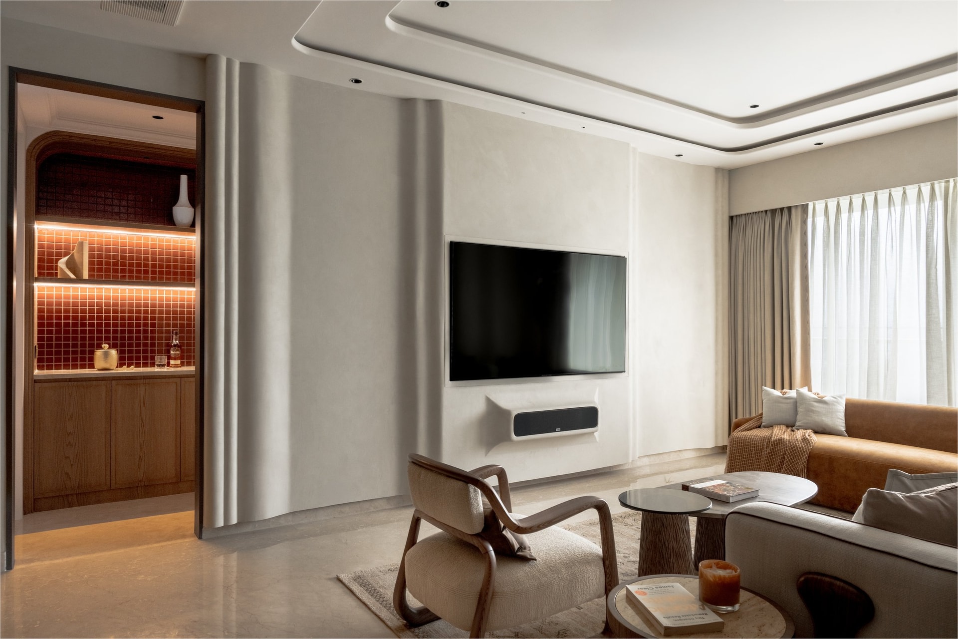 The media wall in soft plaster, with the oxblood-tiled bar niche providing the apartment's single saturated note