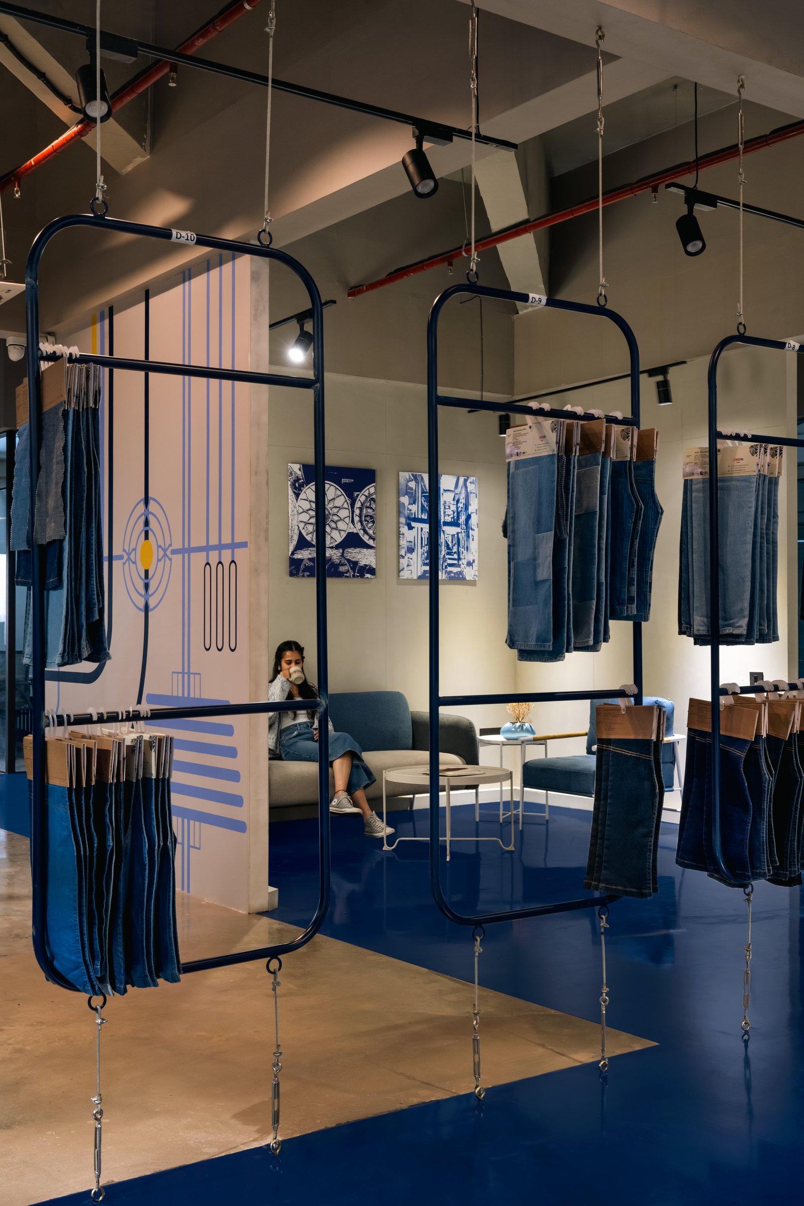 A view through the central display gallery, where indigo-framed modular screens suspended on steel cables hold denim at eye level and shape a labyrinthine route