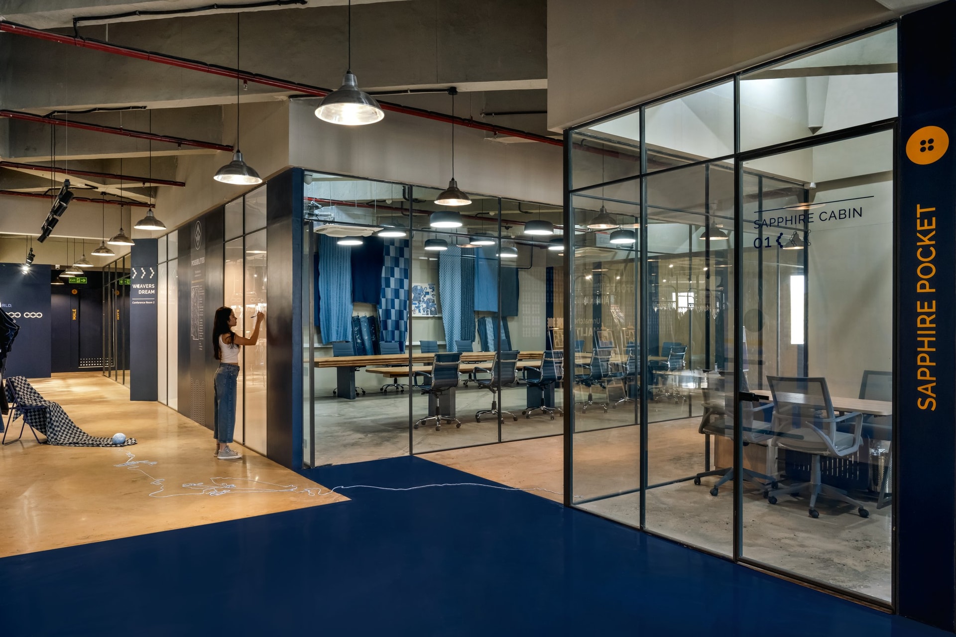 The Sapphire Cabin meeting room, where hanging denim panels inside a glass-walled enclosure continue the display into the working space