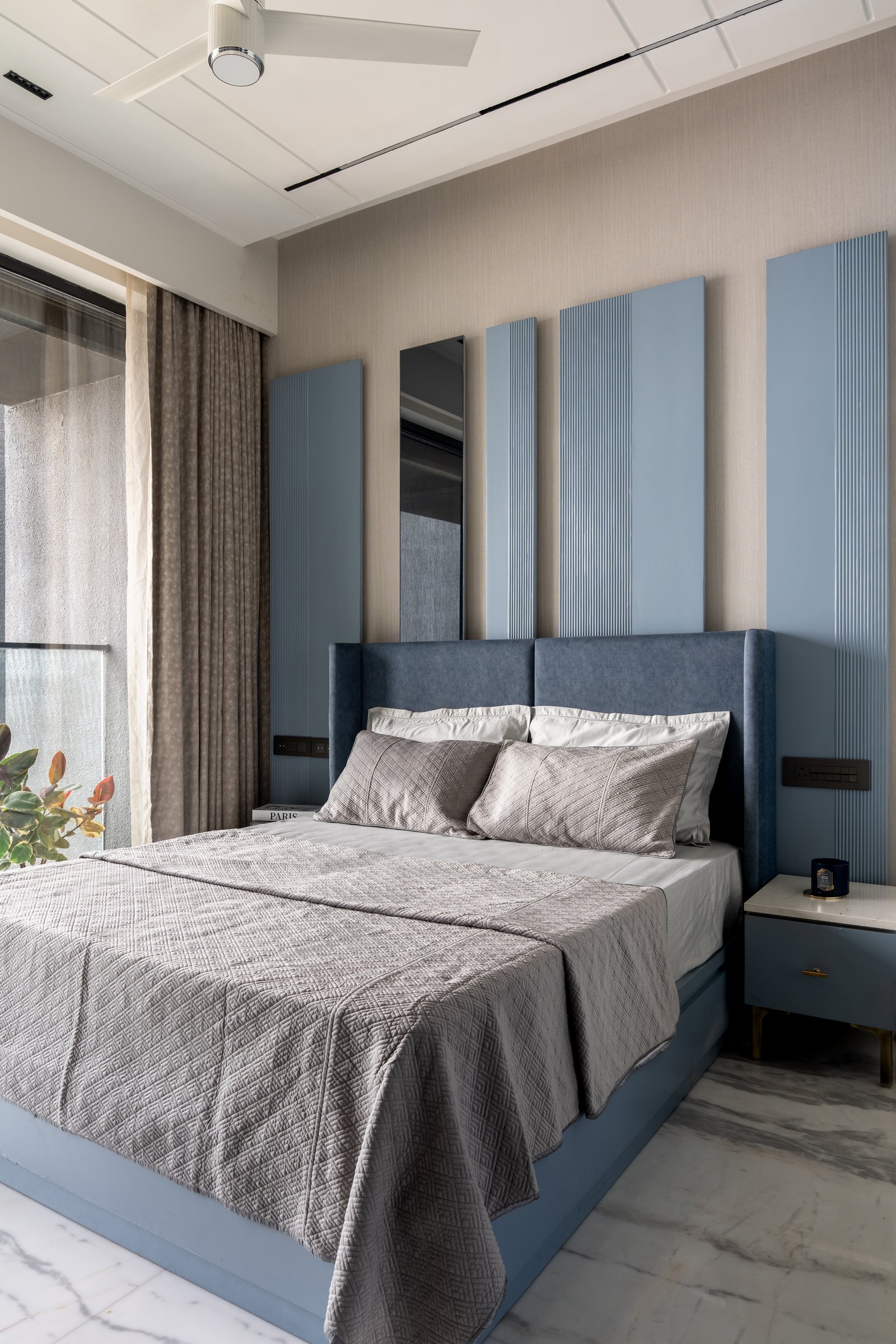 The guest bedroom, where a muted blue headboard sits against alternating fluted and flat panels with a slim inset mirror