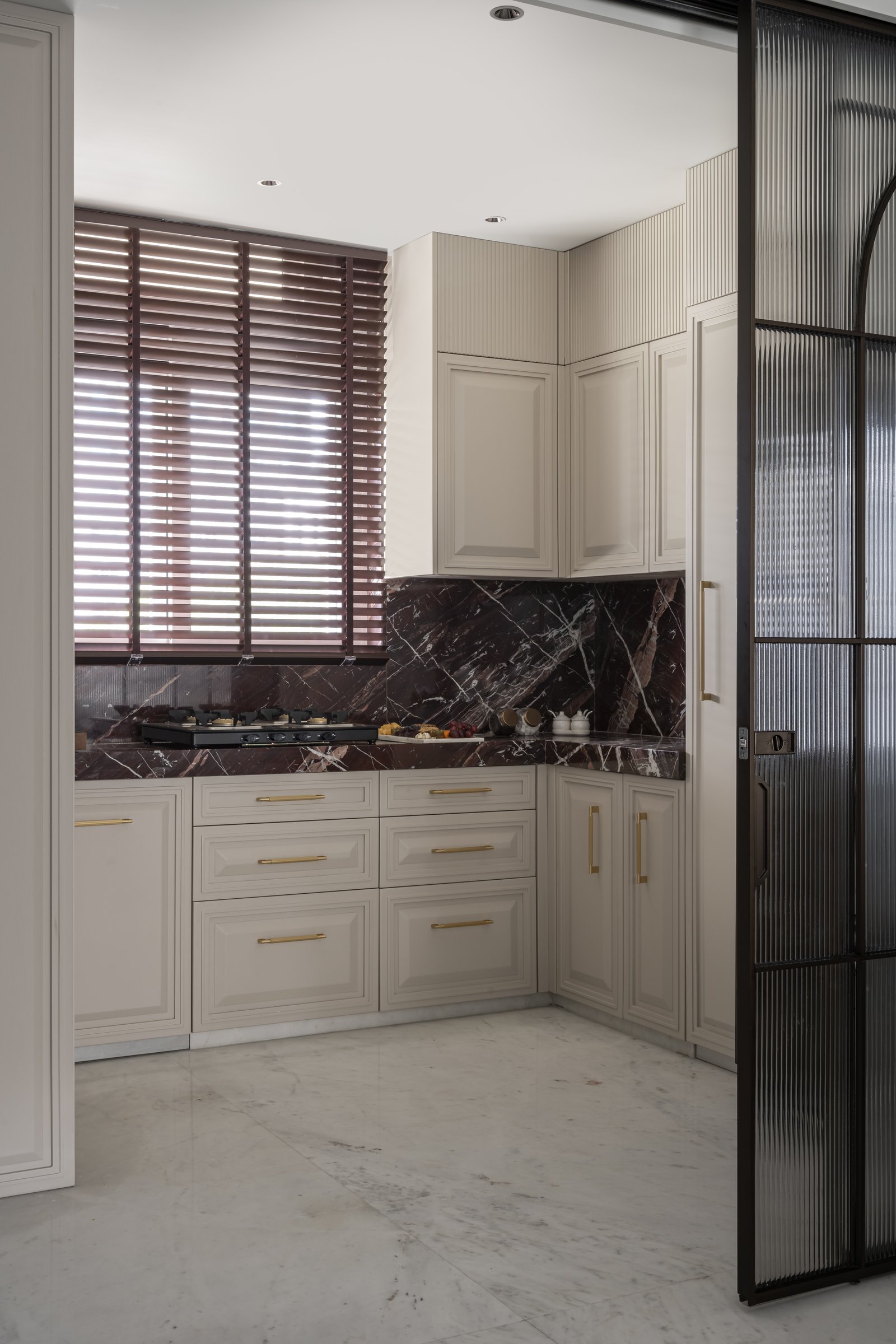 The kitchen, where panelled neutral cabinetry meets a deep burgundy marble countertop and backsplash