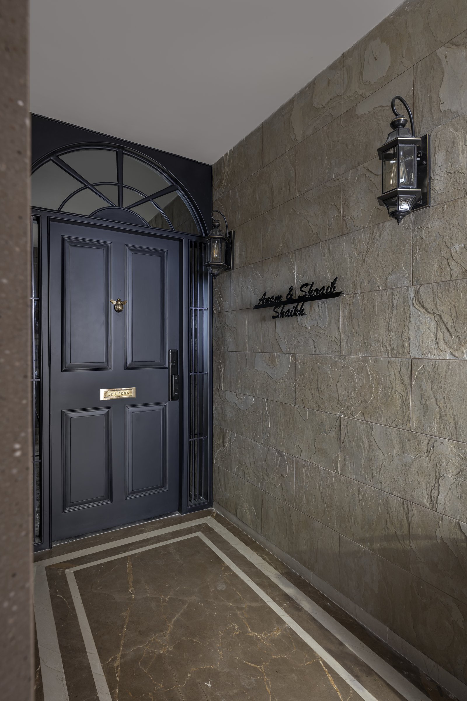 The exterior lobby, where a slate-blue panelled door with a fanlight sits against textured stone cladding