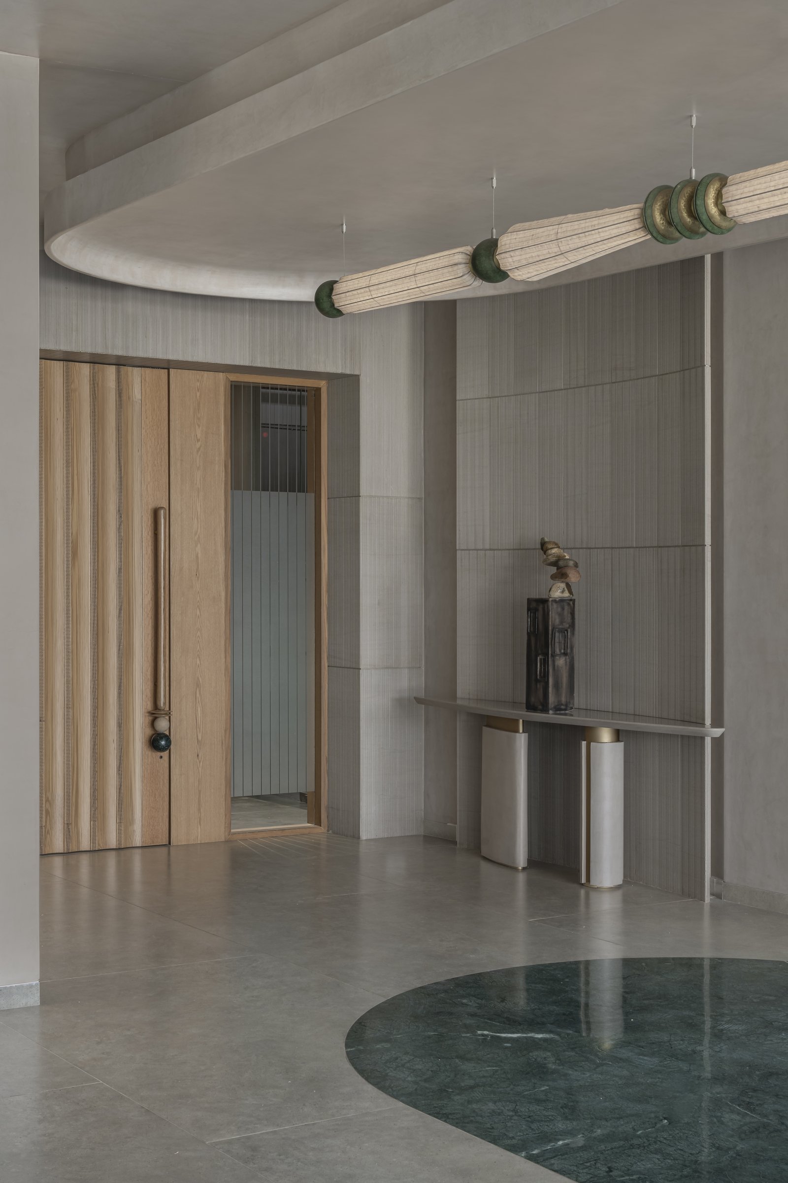 The entry foyer, where a 29-foot sculptural light installation and a dark green marble inlay introduce the office's wabi-sabi palette