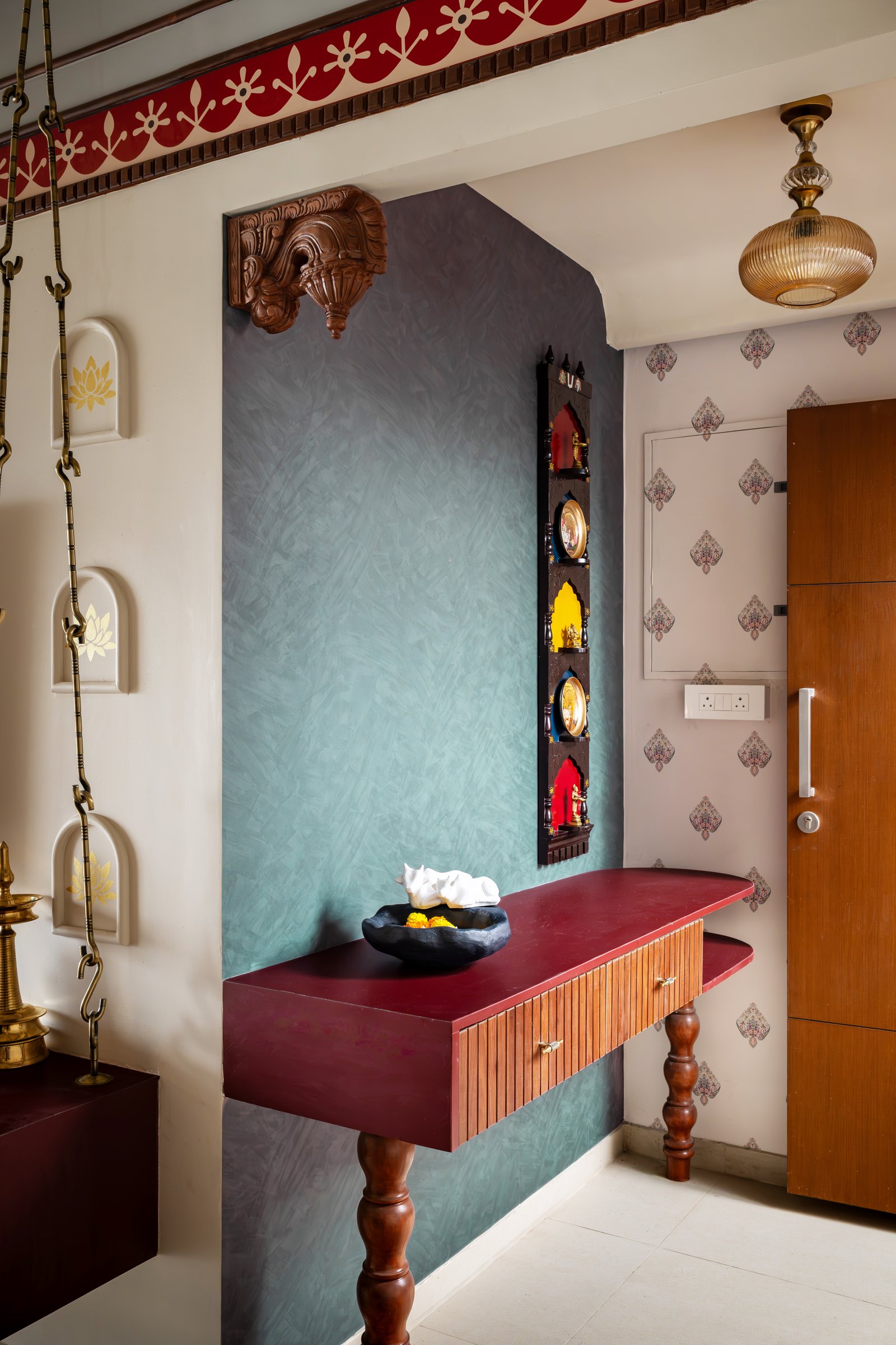 The entrance vignette, where a textured sage-green wall holds a miniature wall shrine above a floating console with turned wooden legs