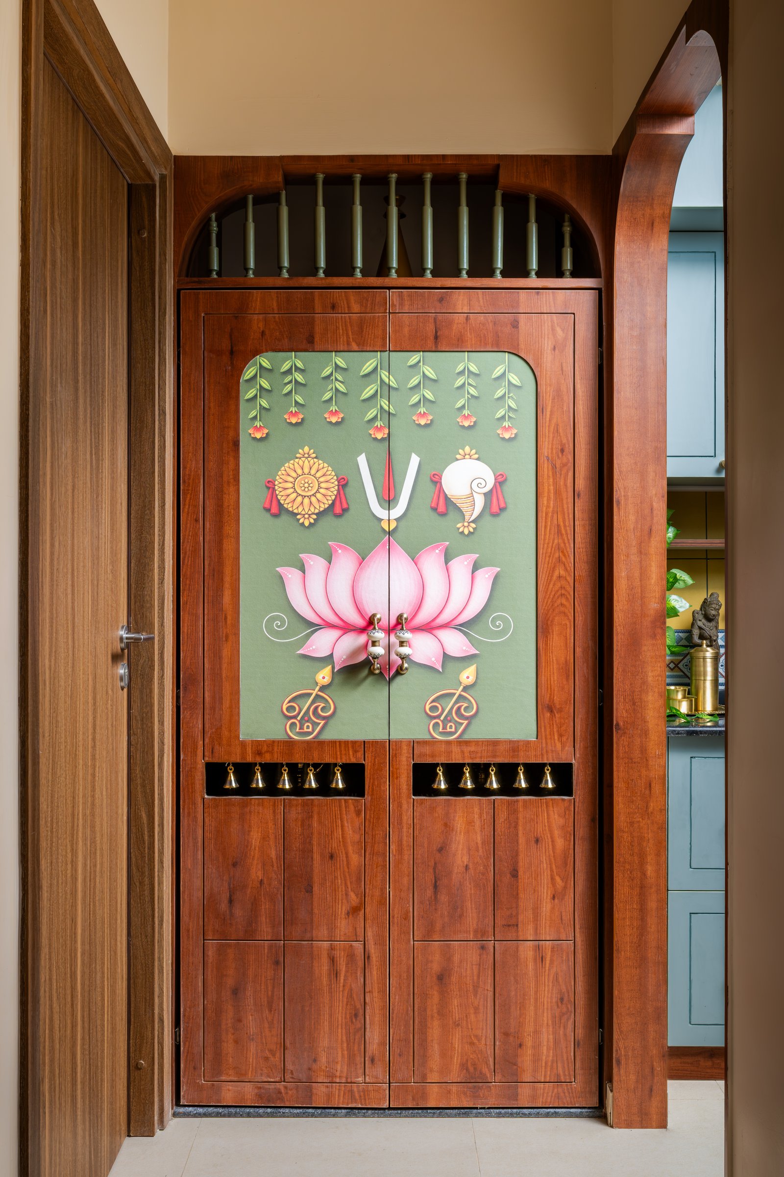 The painted puja doors, with a stylised lotus composition on a sage ground and a row of brass bells along the lower edge