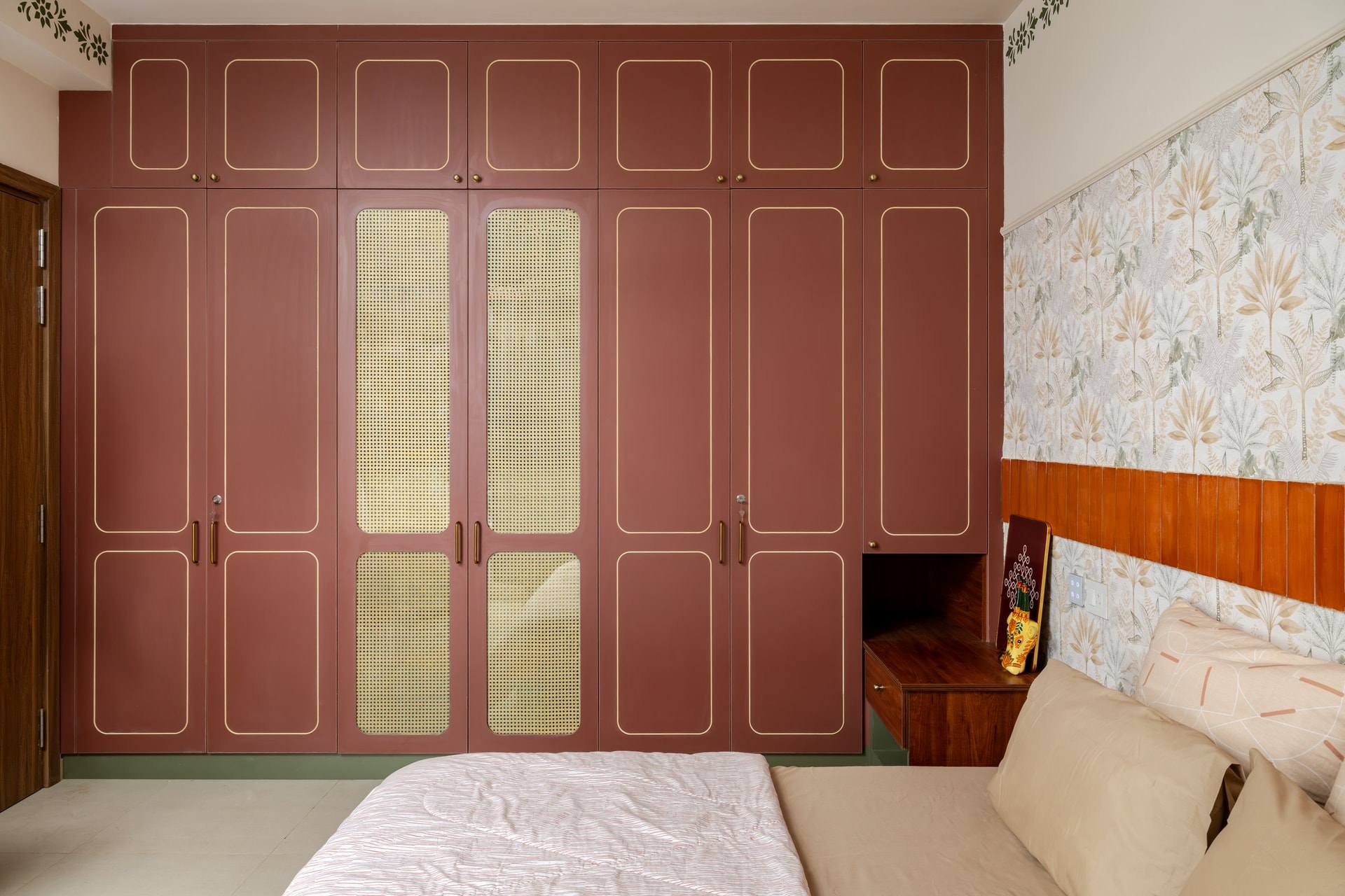 The wardrobe wall, its terracotta fronts and gold outlining framing two tall cane panels at the centre