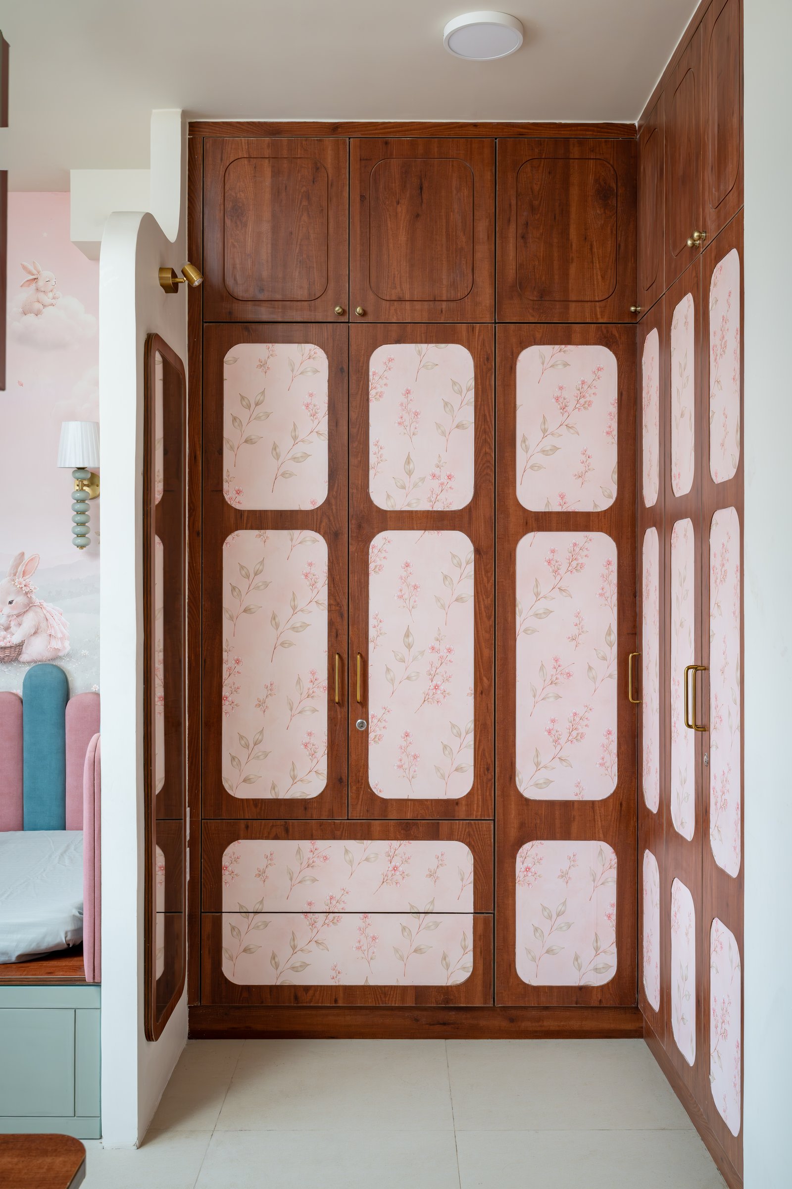 The children's wardrobe, its deep wooden framing surrounding patterned inset panels on a pale blush ground