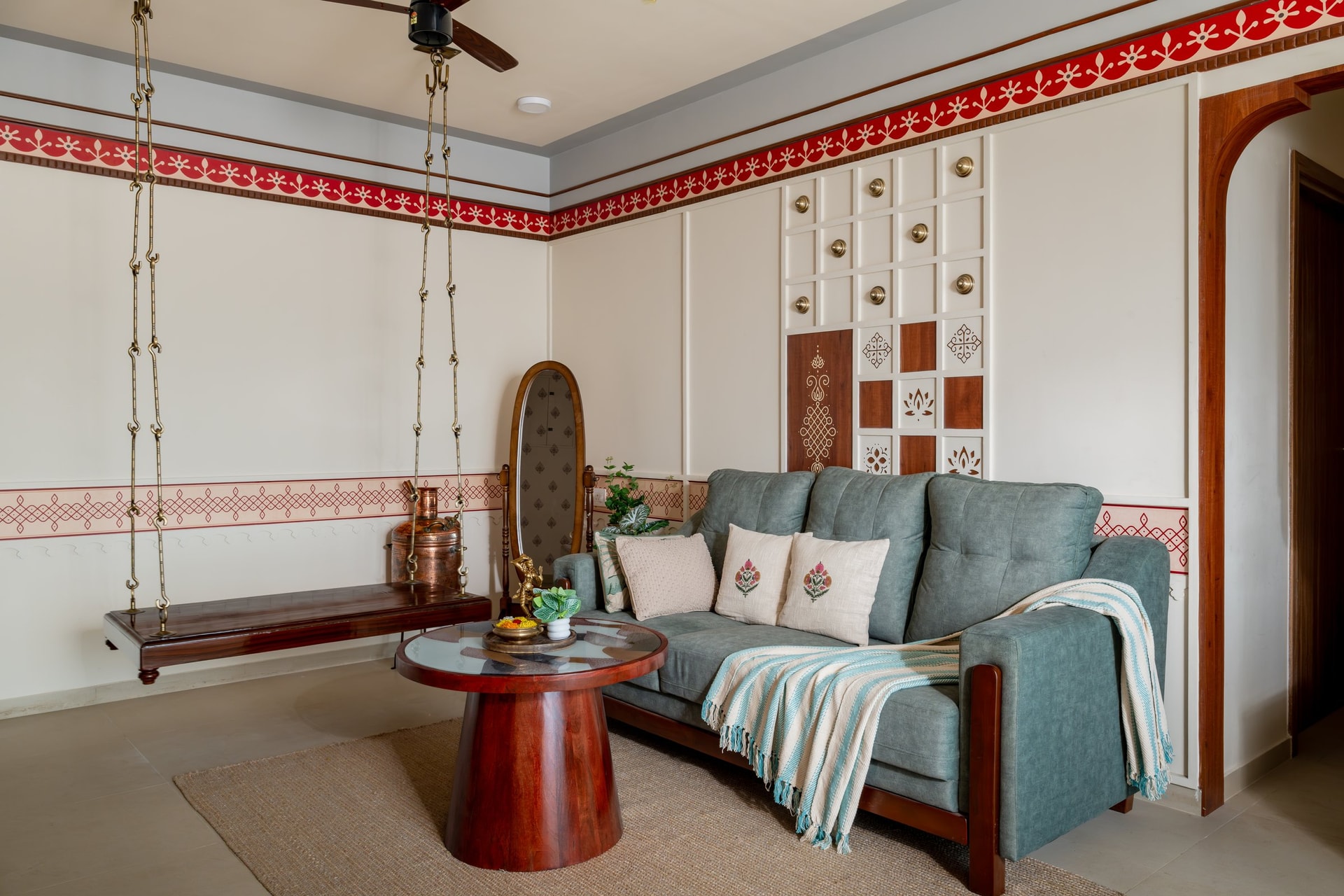 A wider view of the living room, revealing the panelled wall inset with brass medallions and painted kolam motifs behind the sofa