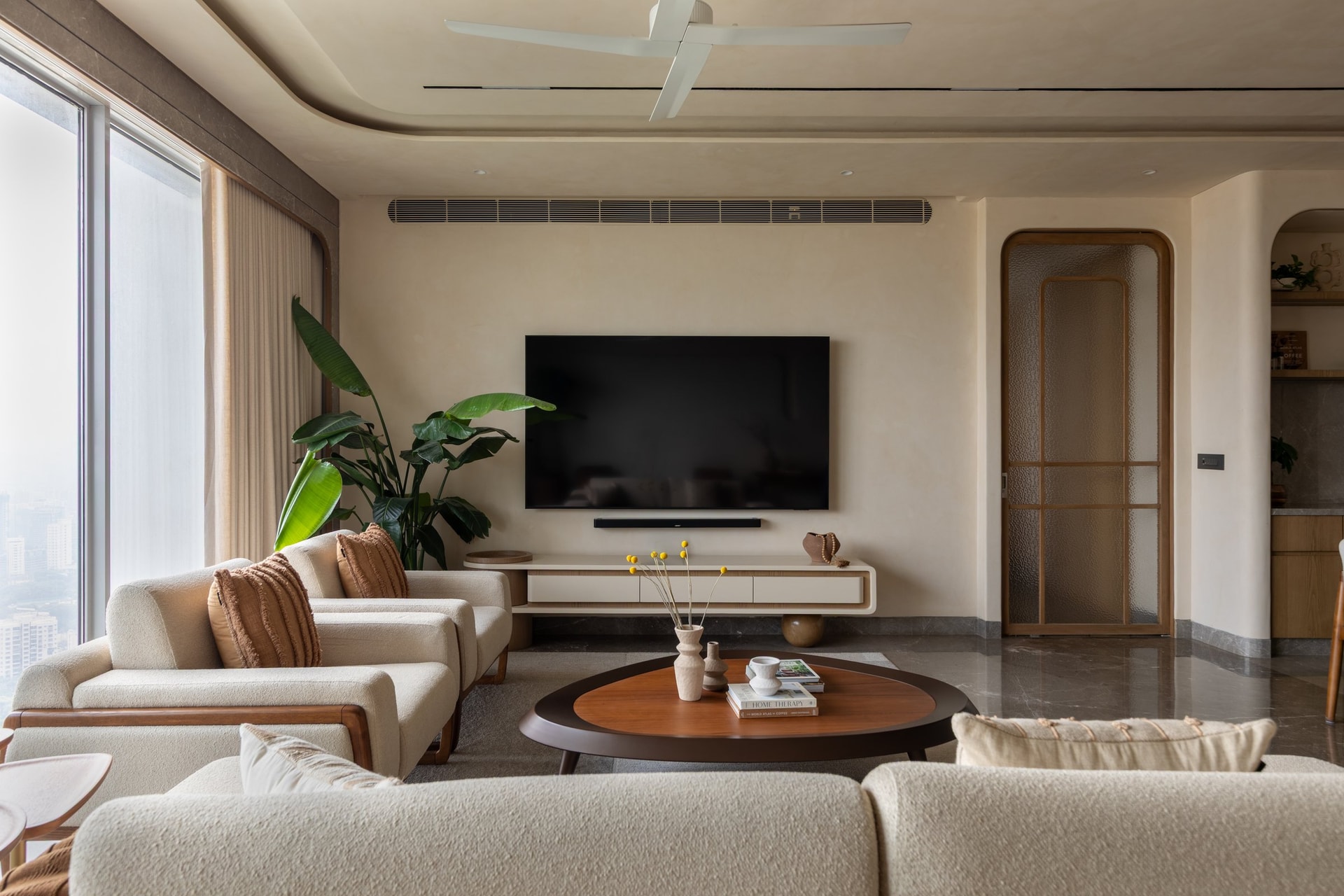 The media wall, where a floating wooden console and an arched reeded-glass door echo the curves introduced at the entry