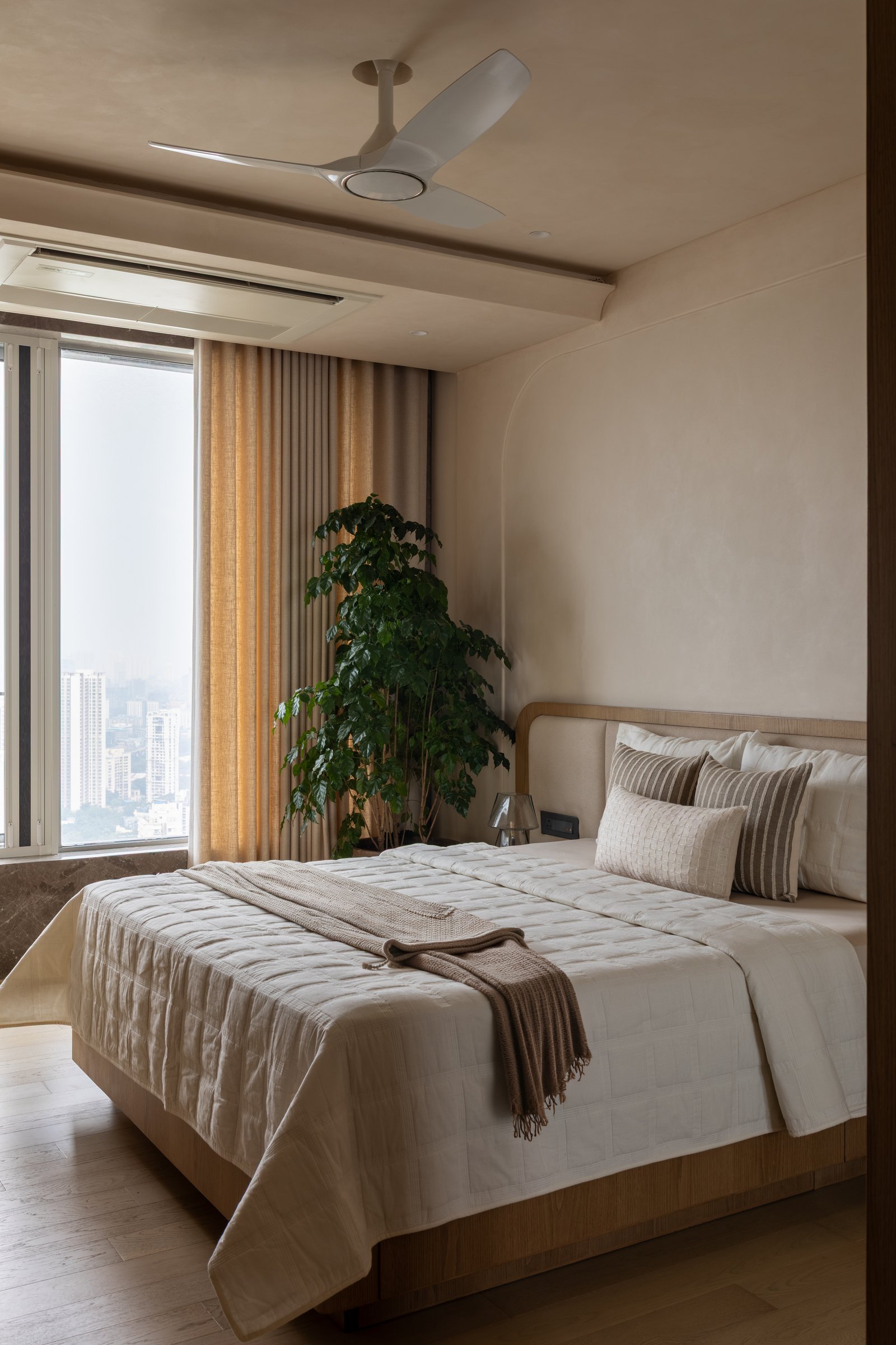 The second bedroom, where a low curved wooden headboard sits against a plastered wall layered with oatmeal and amber drapery