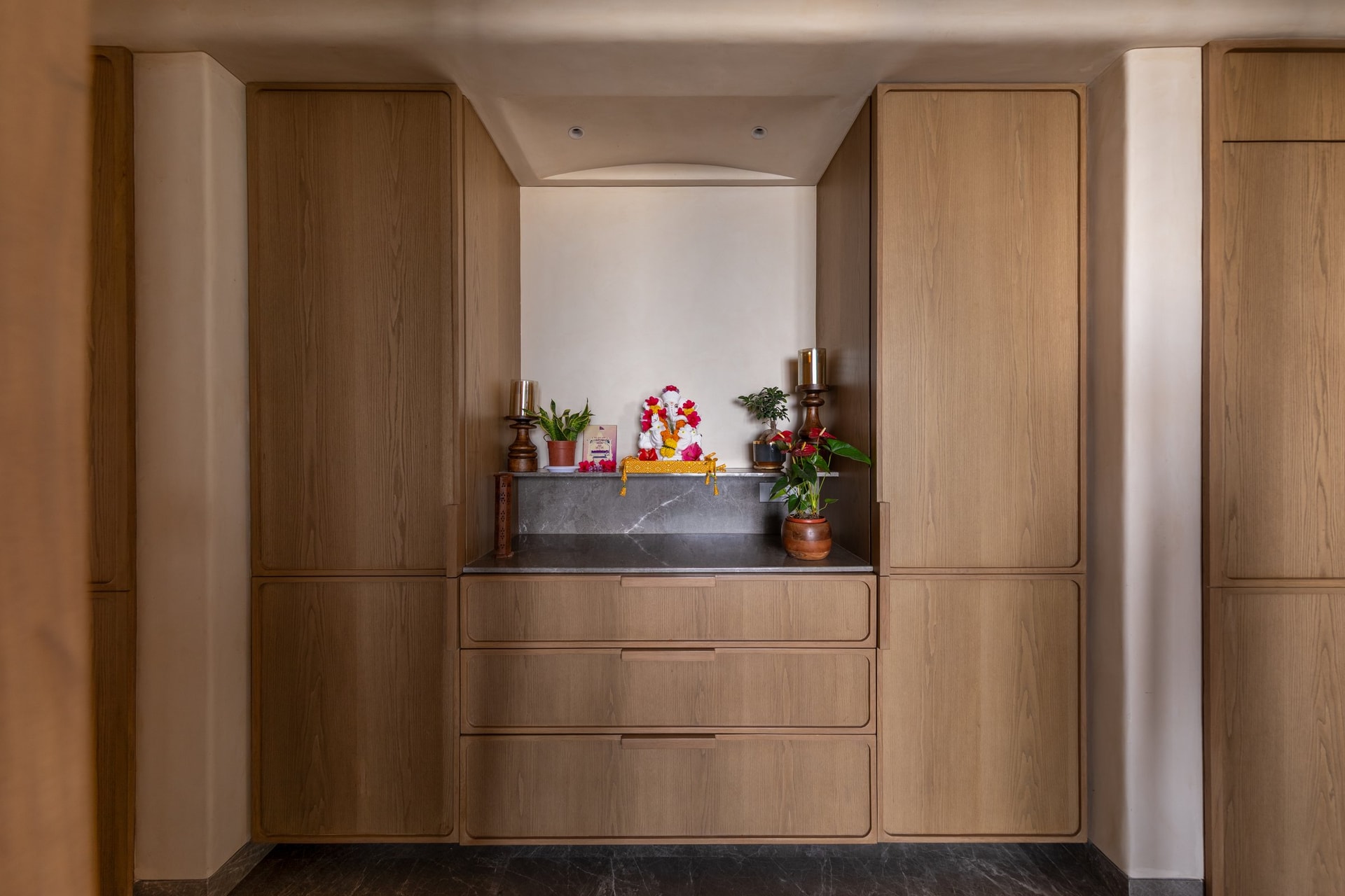 The puja alcove, set within a wall of light veneered joinery and crowned by a softly curved recess