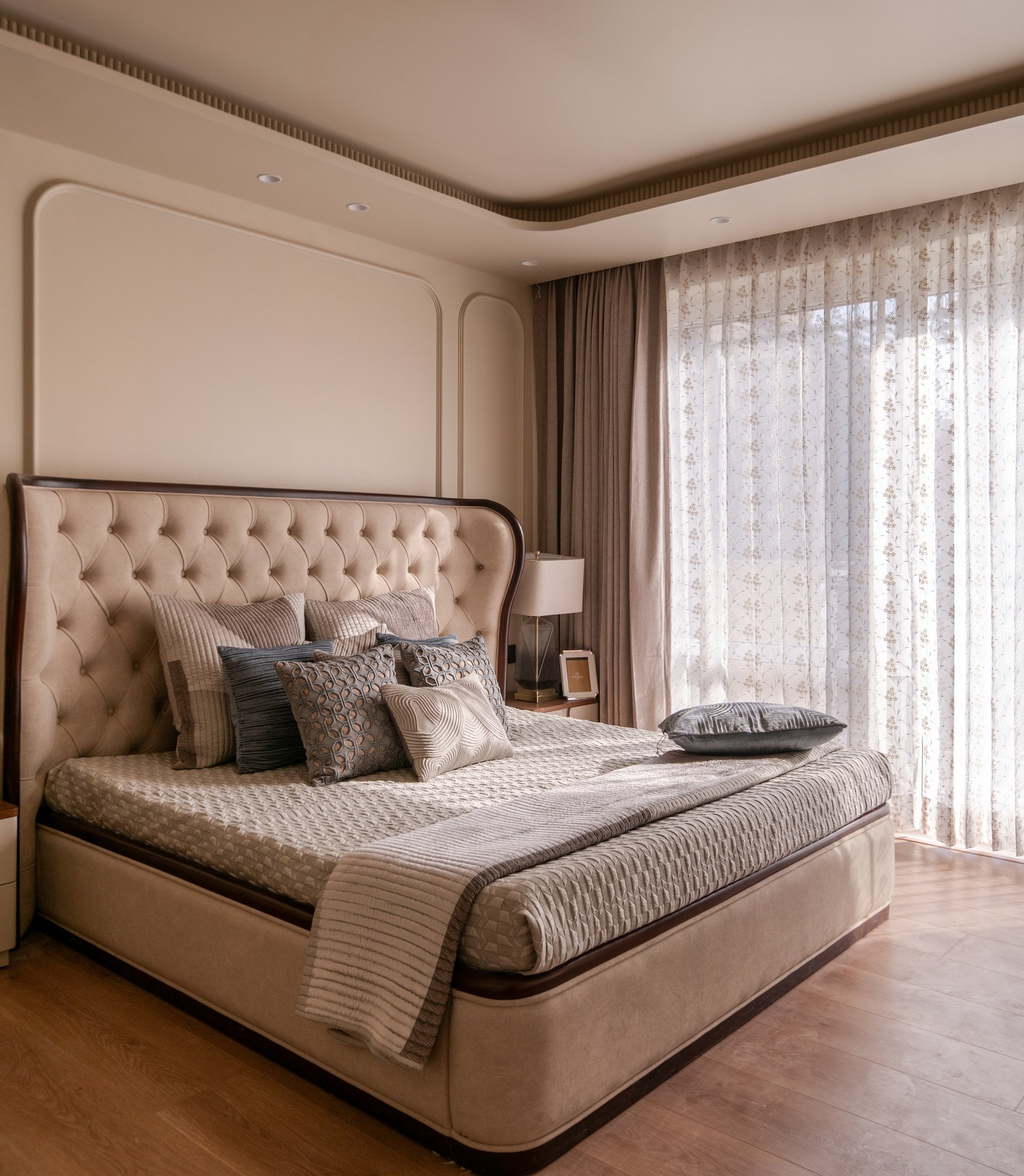The master bedroom, where a curved tufted headboard in dark wood sits against a wall of recessed arched moulding