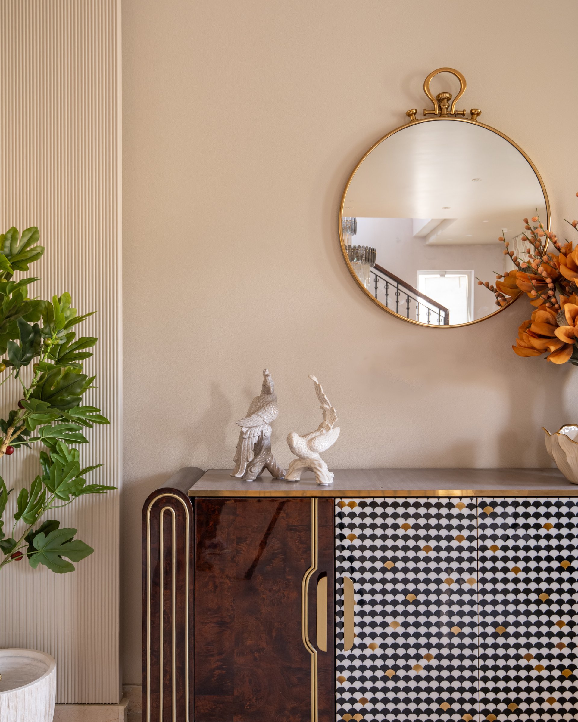 The foyer vignette: a lacquered burlwood console with scalloped inlay set beneath a brass-rimmed circular mirror