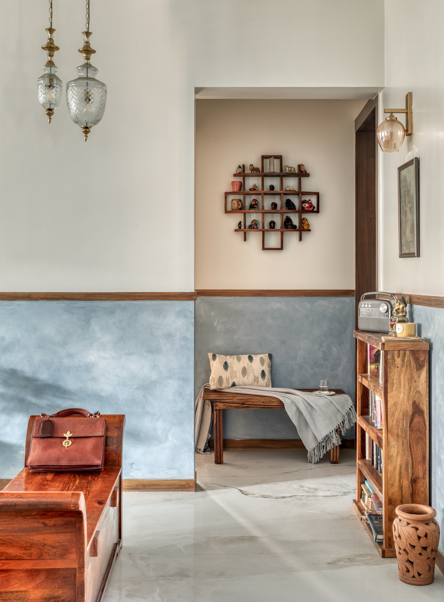 A reading nook and curio shelf in the foyer zone, framed by the two-tone plaster treatment that runs through the apartment
