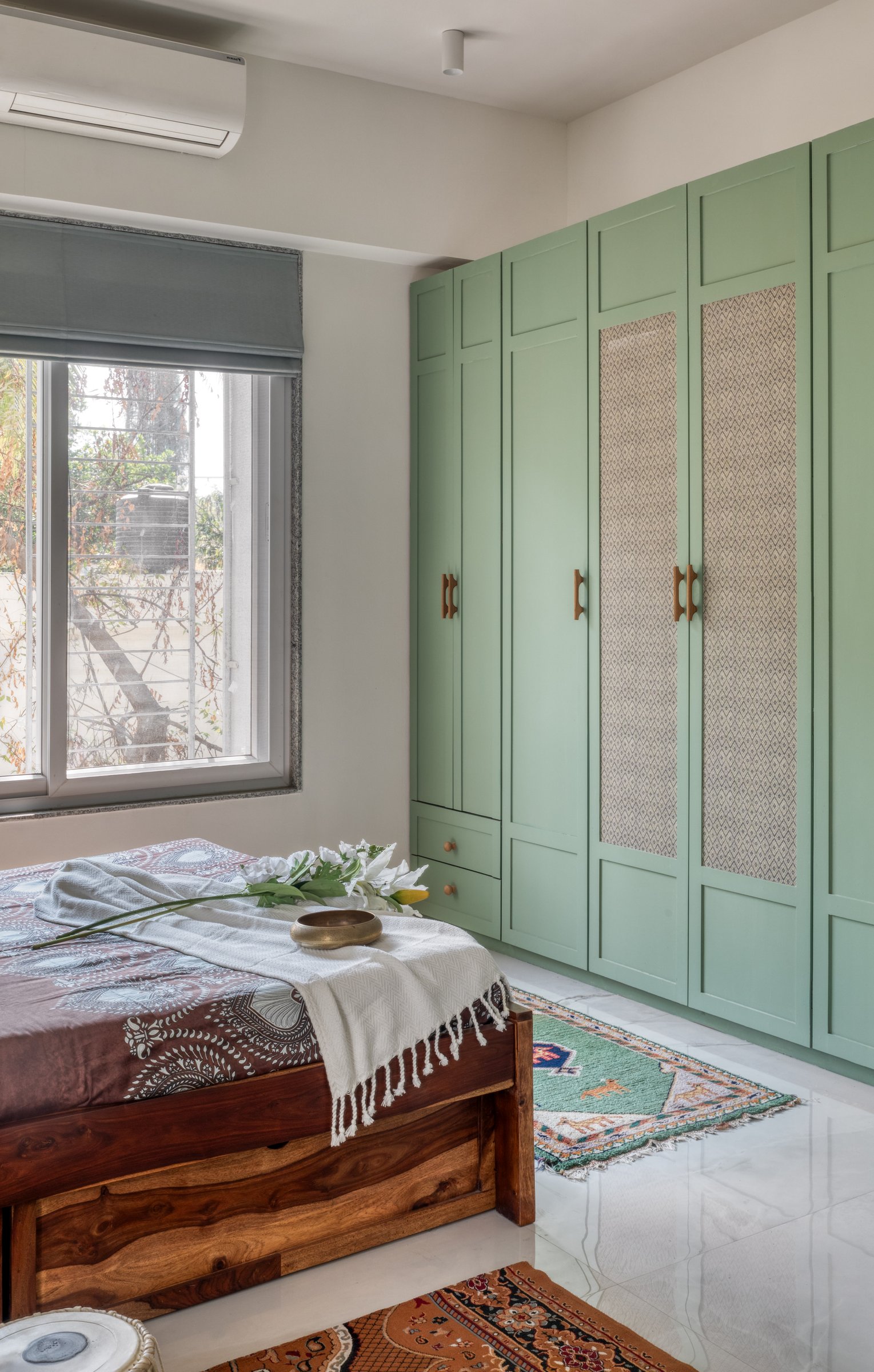Sage green wardrobes with woven-texture inserts and brass handles, giving storage the presence of a craft object