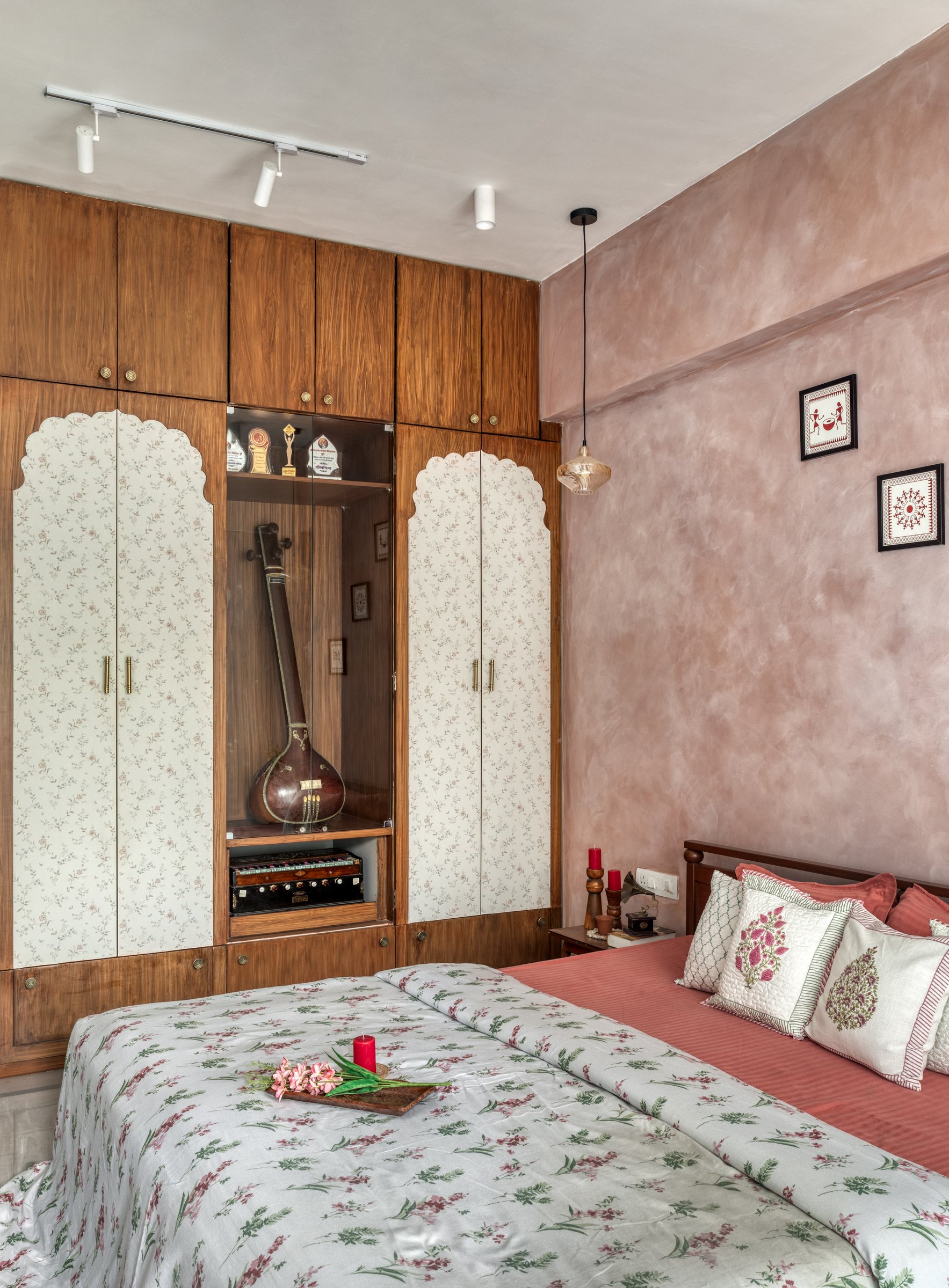 The master bedroom's wardrobe wall, where scalloped-arch panels frame a glass vitrine housing a sitar and harmonium