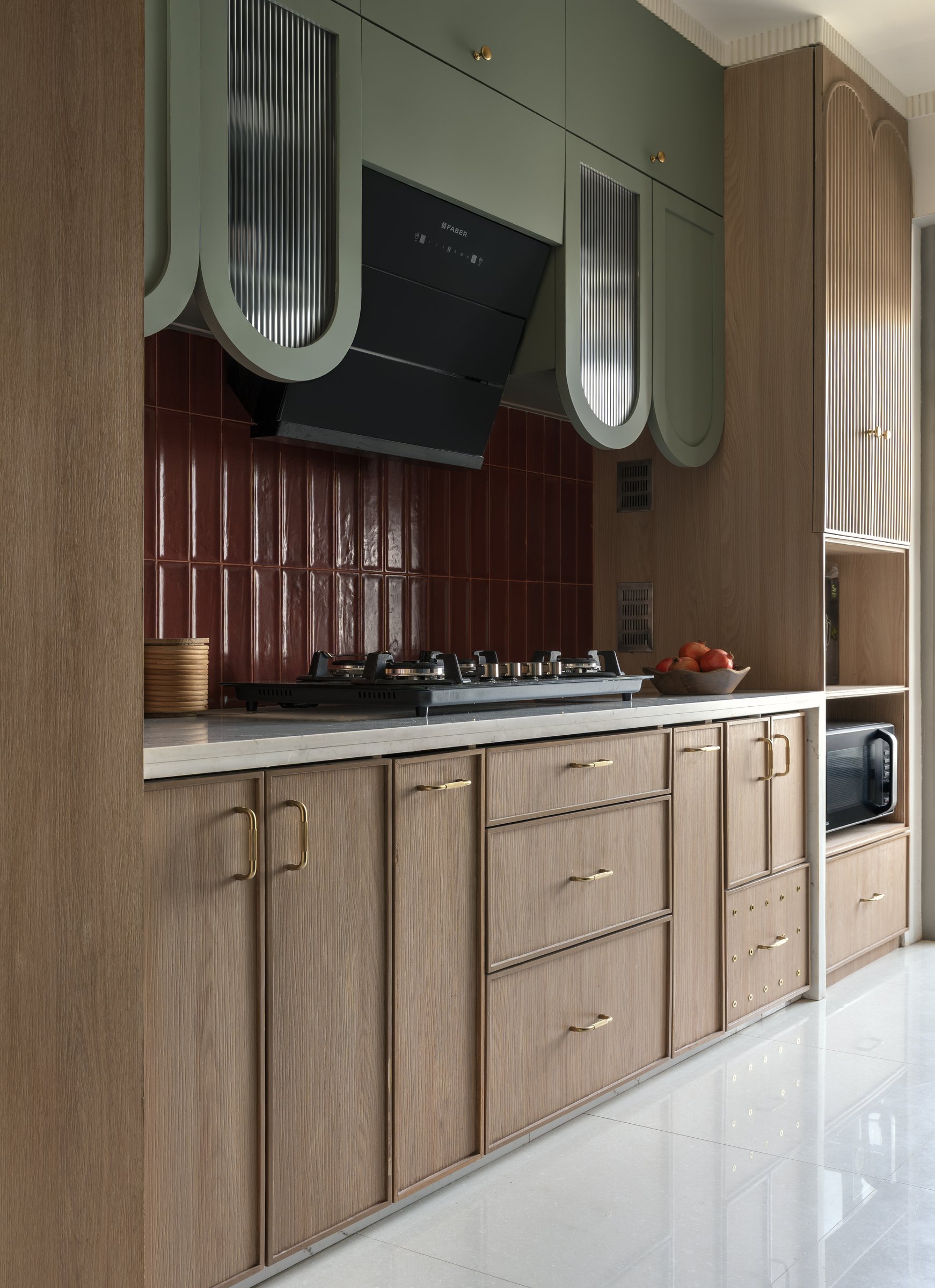 The kitchen pairs sage cabinetry, oxblood tile and blond ash with a confidence that reads as period-referencing rather than pastiche