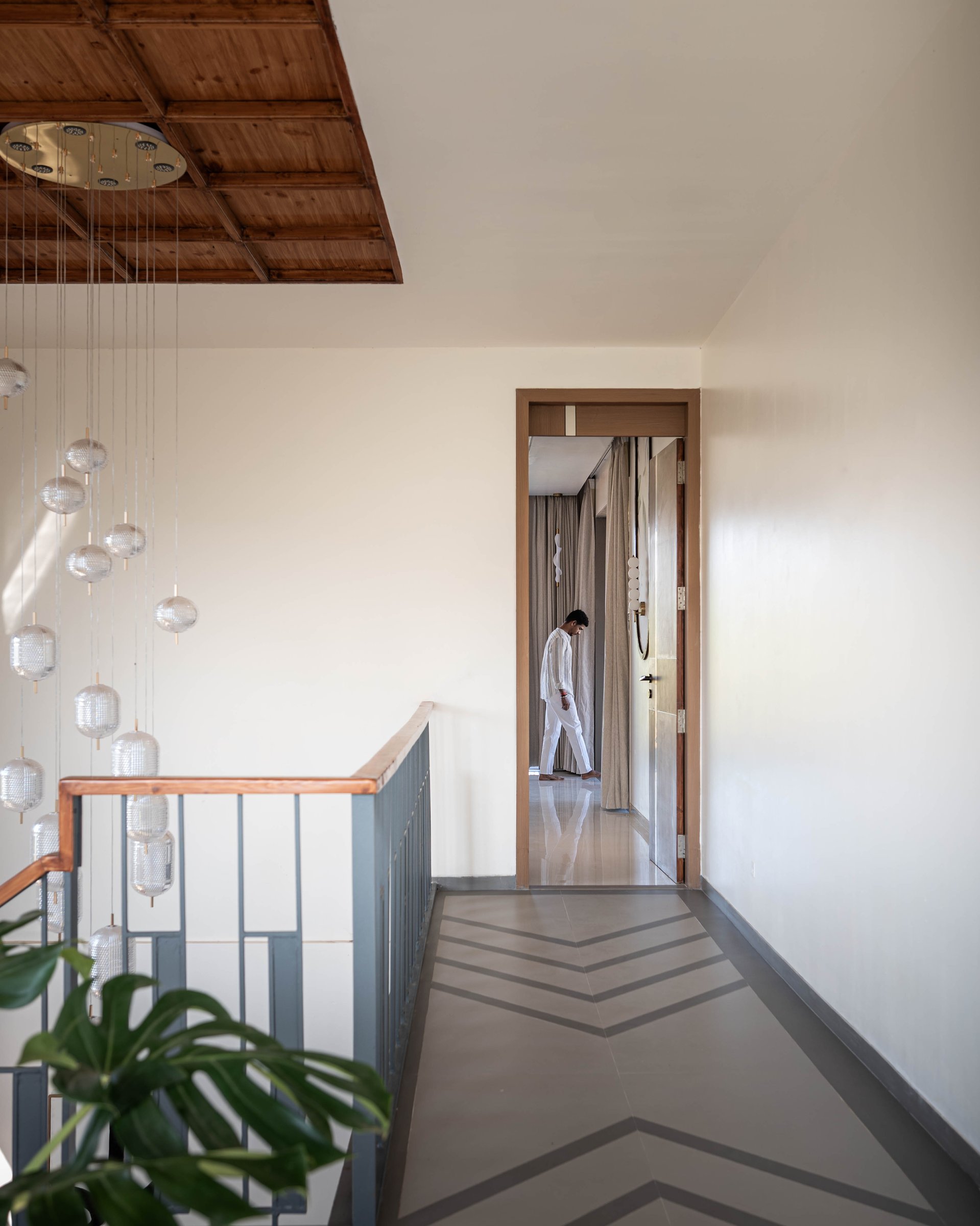 The upper corridor: chevron flooring, a cascading glass-globe chandelier, and a timber-panelled ceiling