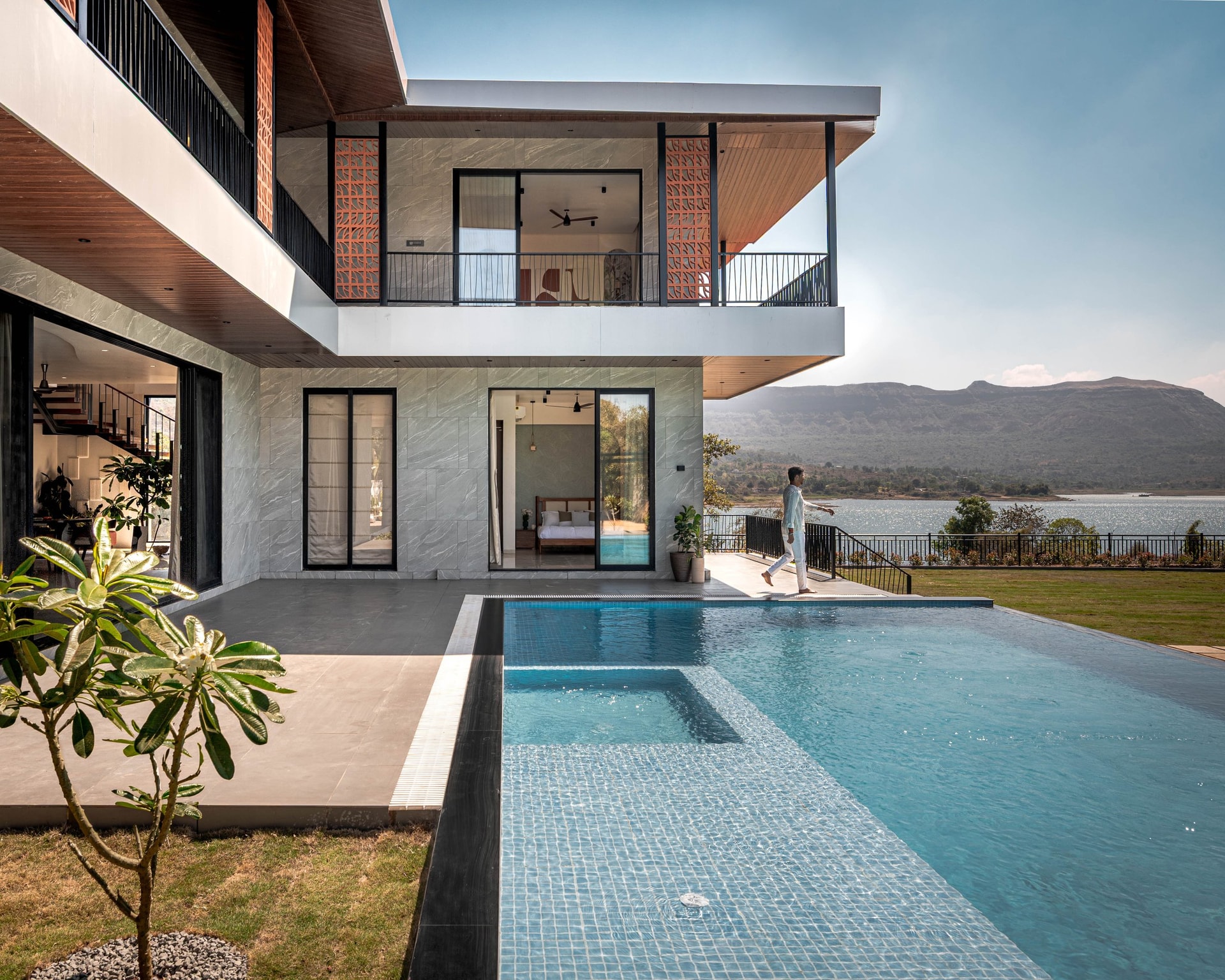 The villa from the garden: steel frame, stone cladding, terracotta screens, and the pool extending toward the reservoir
