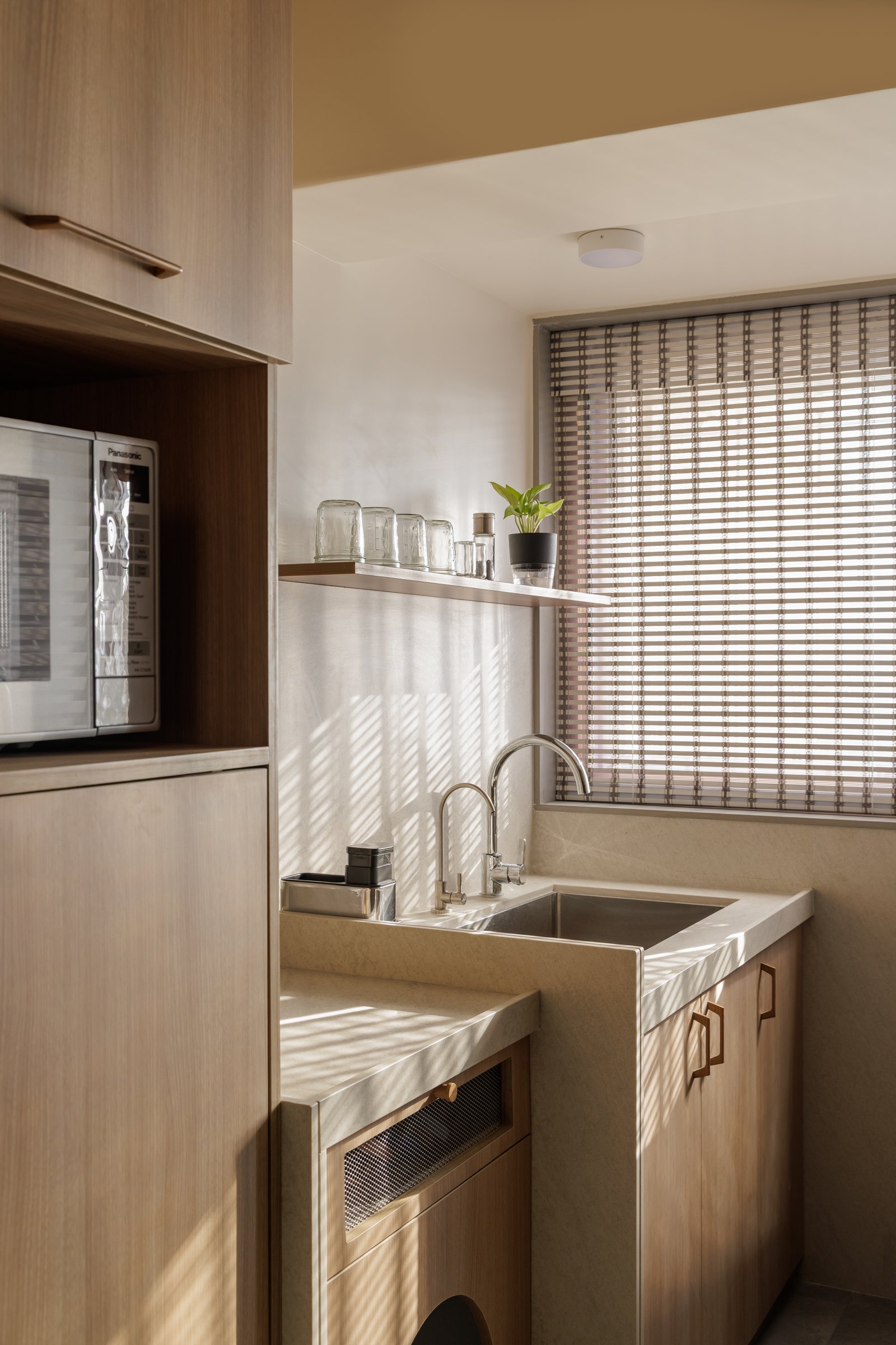 The utility corner: a woven blind filters afternoon light across upturned glasses and a single potted plant