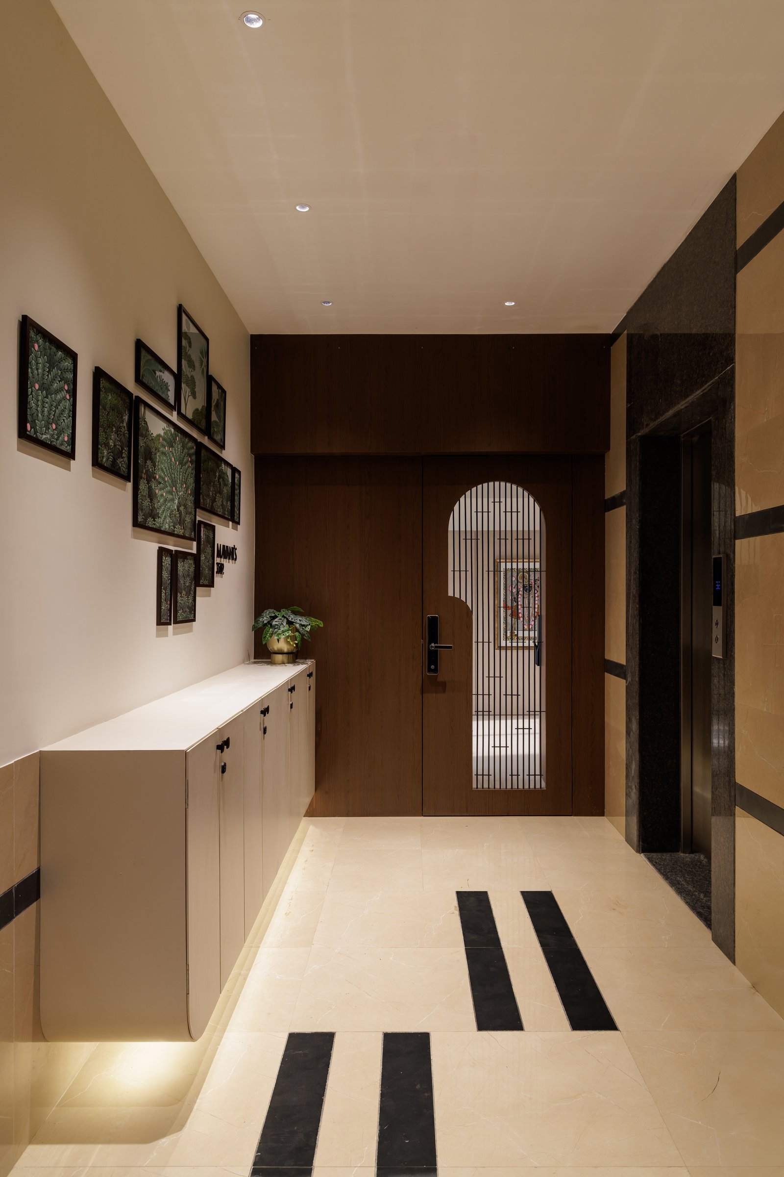 The foyer: floating cabinetry, inset black floor bands, and an arched grille door that frames the home before it begins