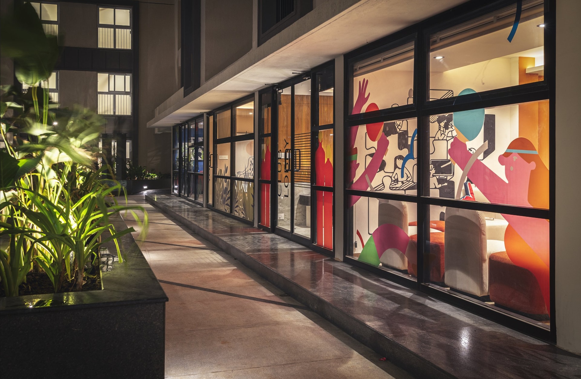 The glazed corridor at night, where sun-film artwork turns the facade into a quiet announcement