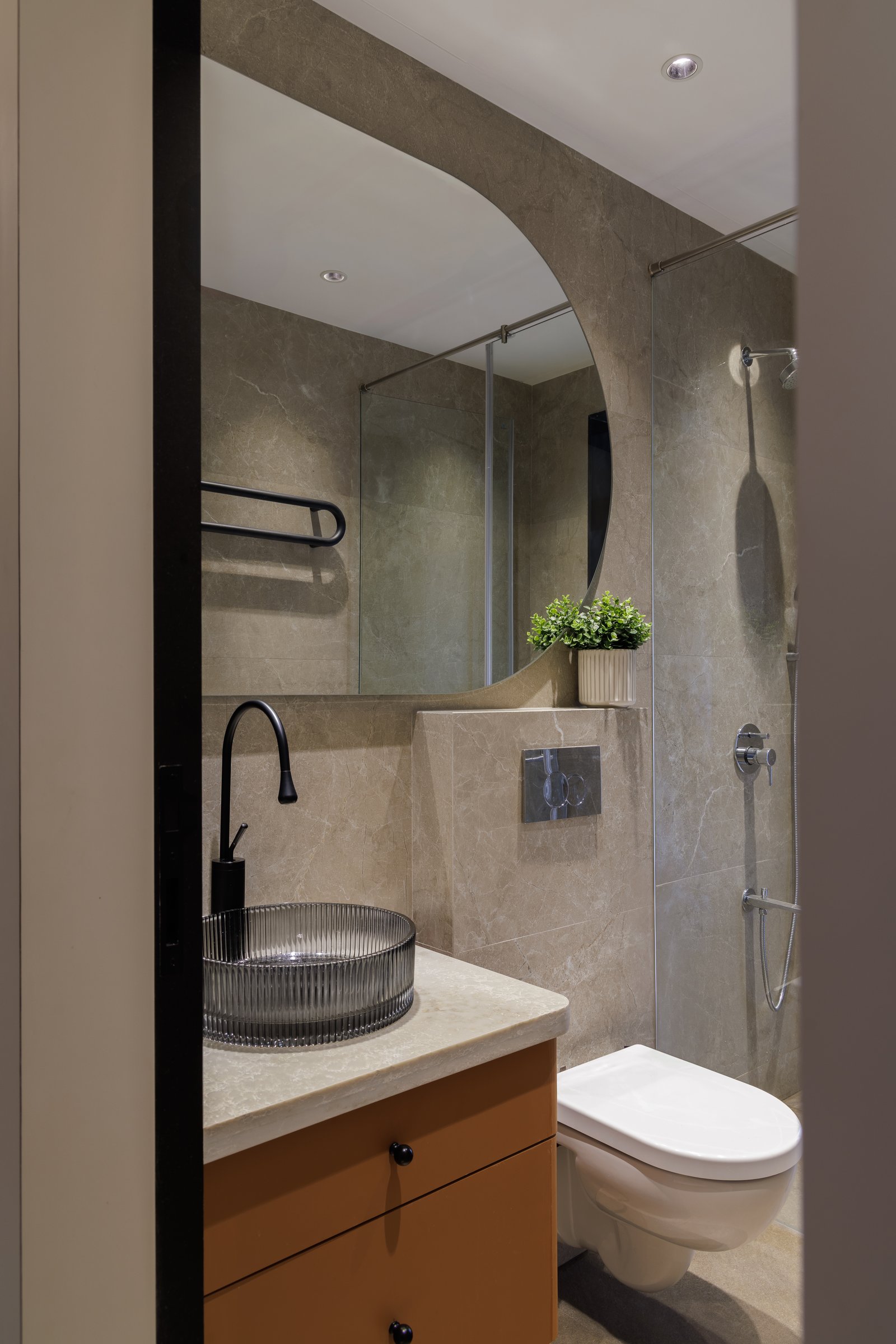 The son's bathroom: an arched mirror set into taupe stone above a burnt orange vanity
