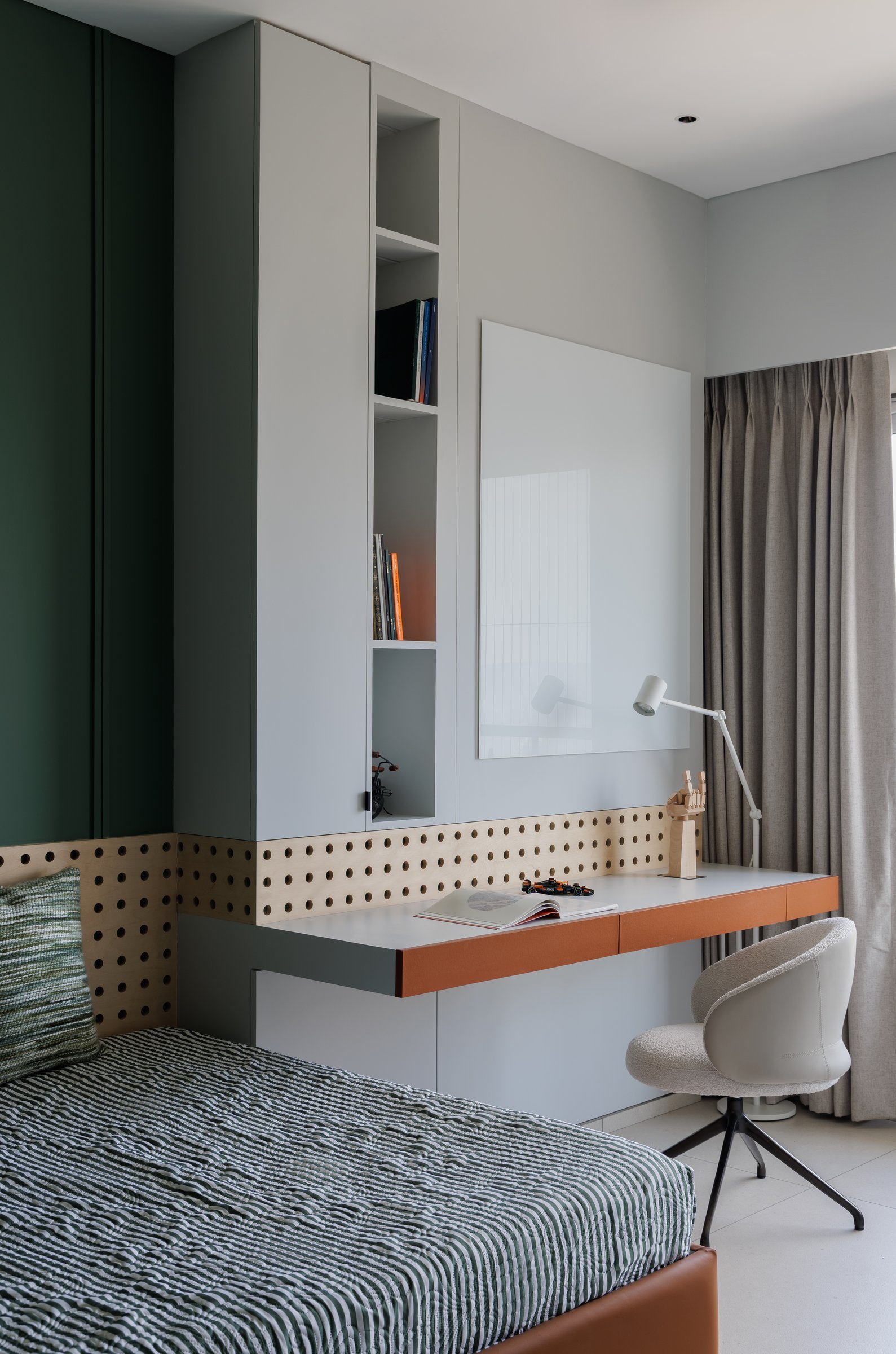 The study side of the same room: a floating desk in cream and tan beneath a perforated birch pinboard