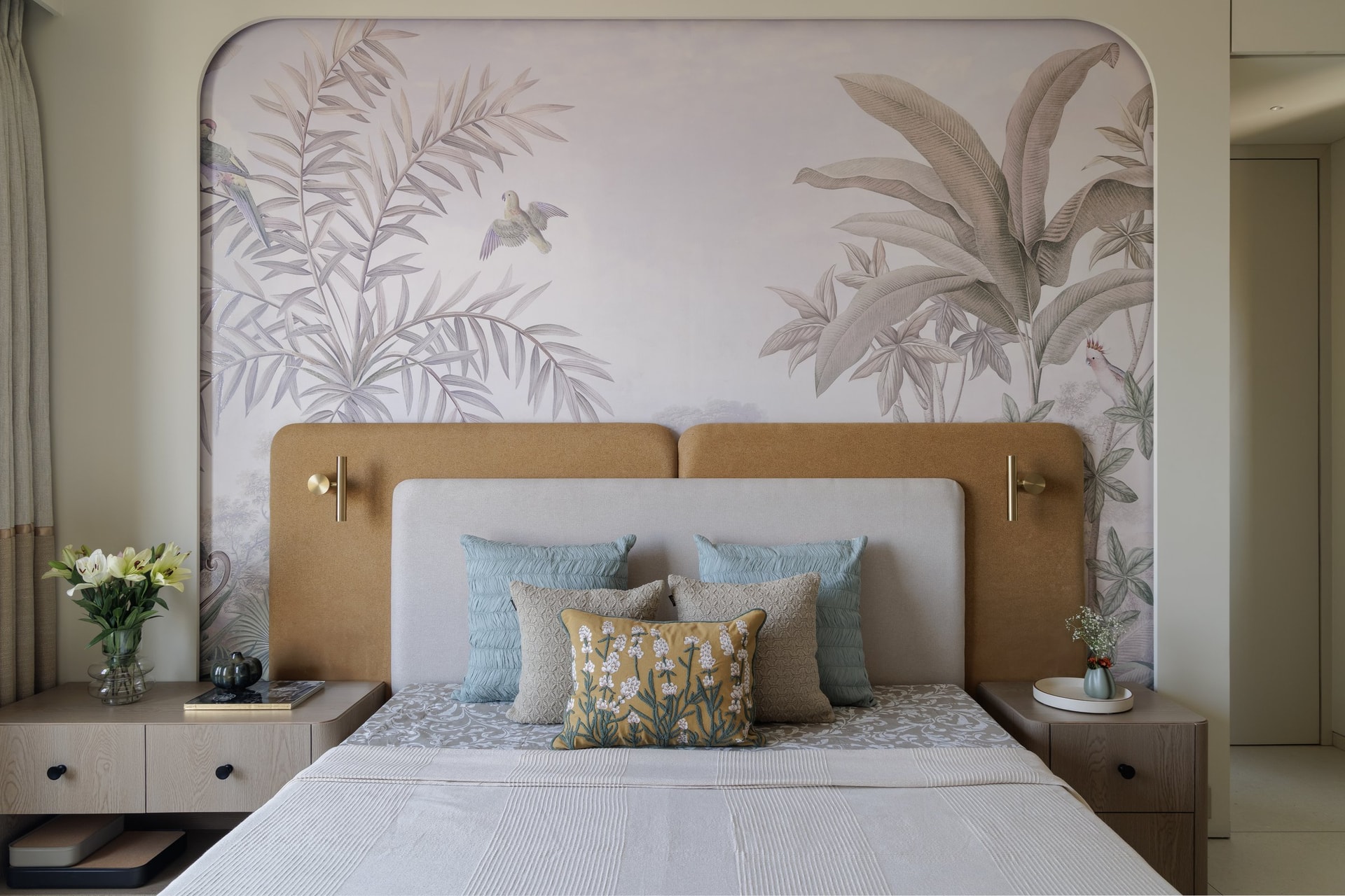 In the master bedroom, an arched mural of pale palms and birds rises behind a layered headboard composition