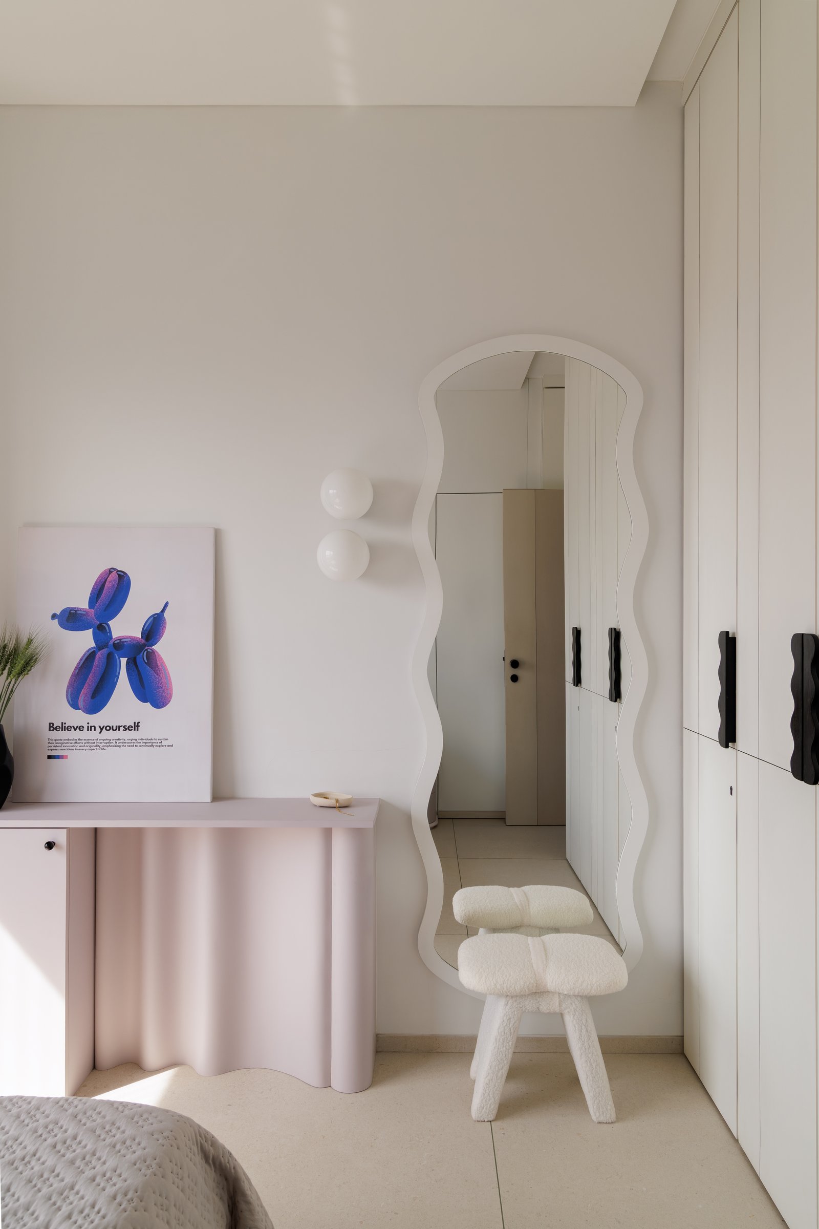 A wavy-edged mirror and undulating blush console anchor the dressing corner