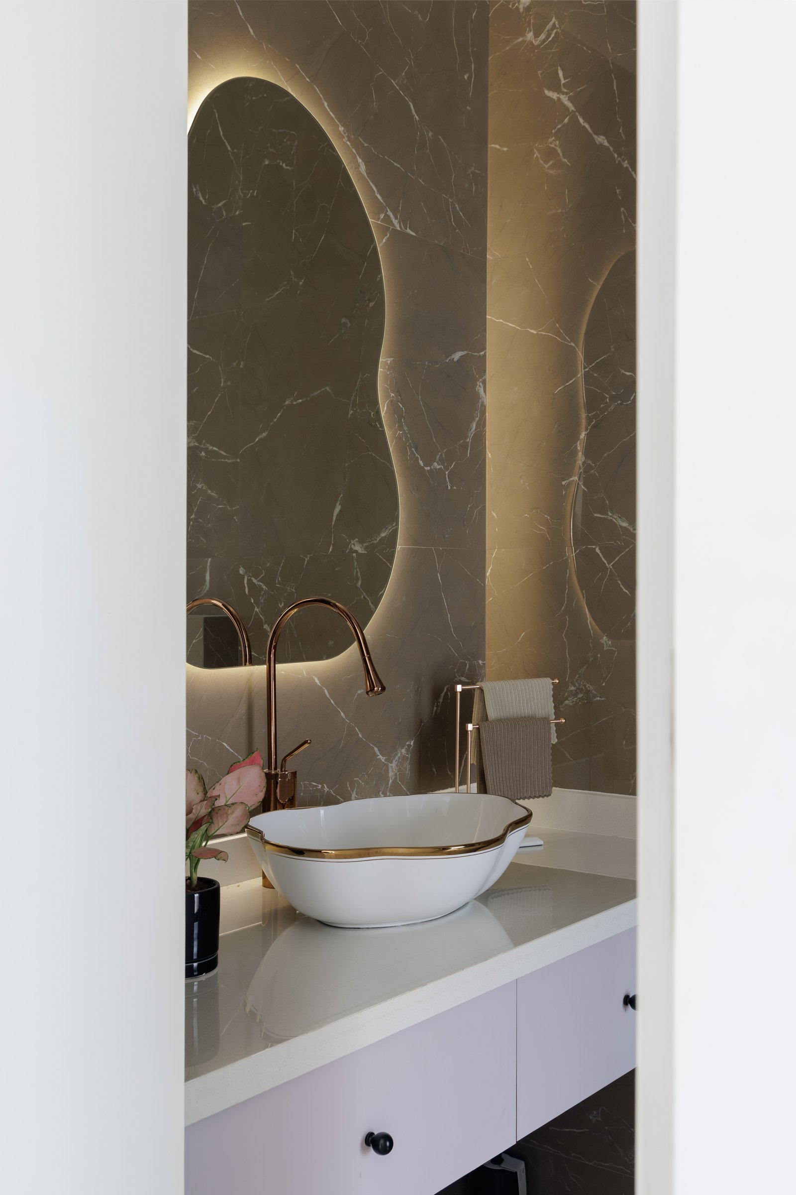 The daughter's powder room, where a backlit pebble mirror and a scalloped basin earn their indulgence
