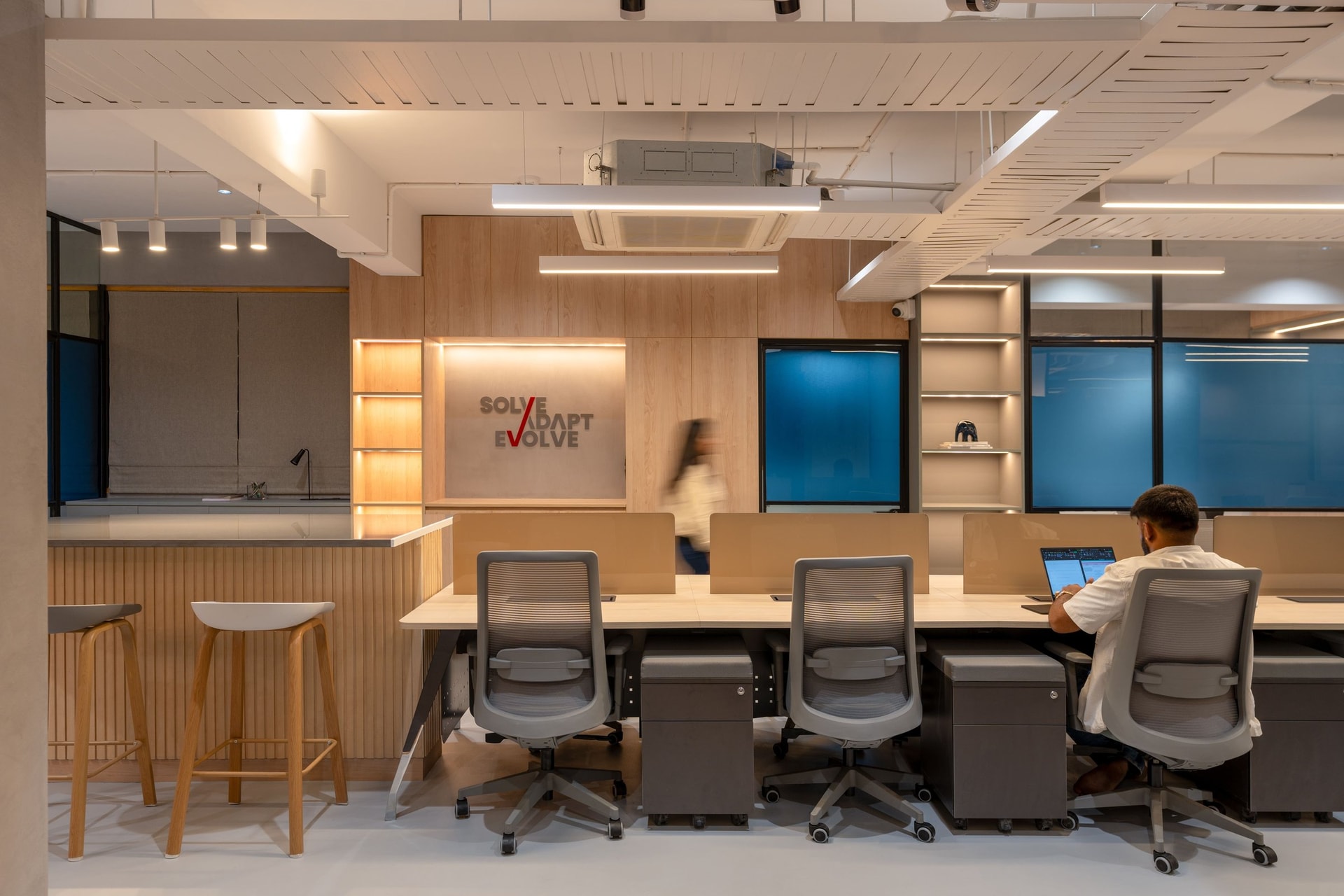 A slatted wood ceiling raft softens the industrial ceiling and conceals services above the second workstation cluster