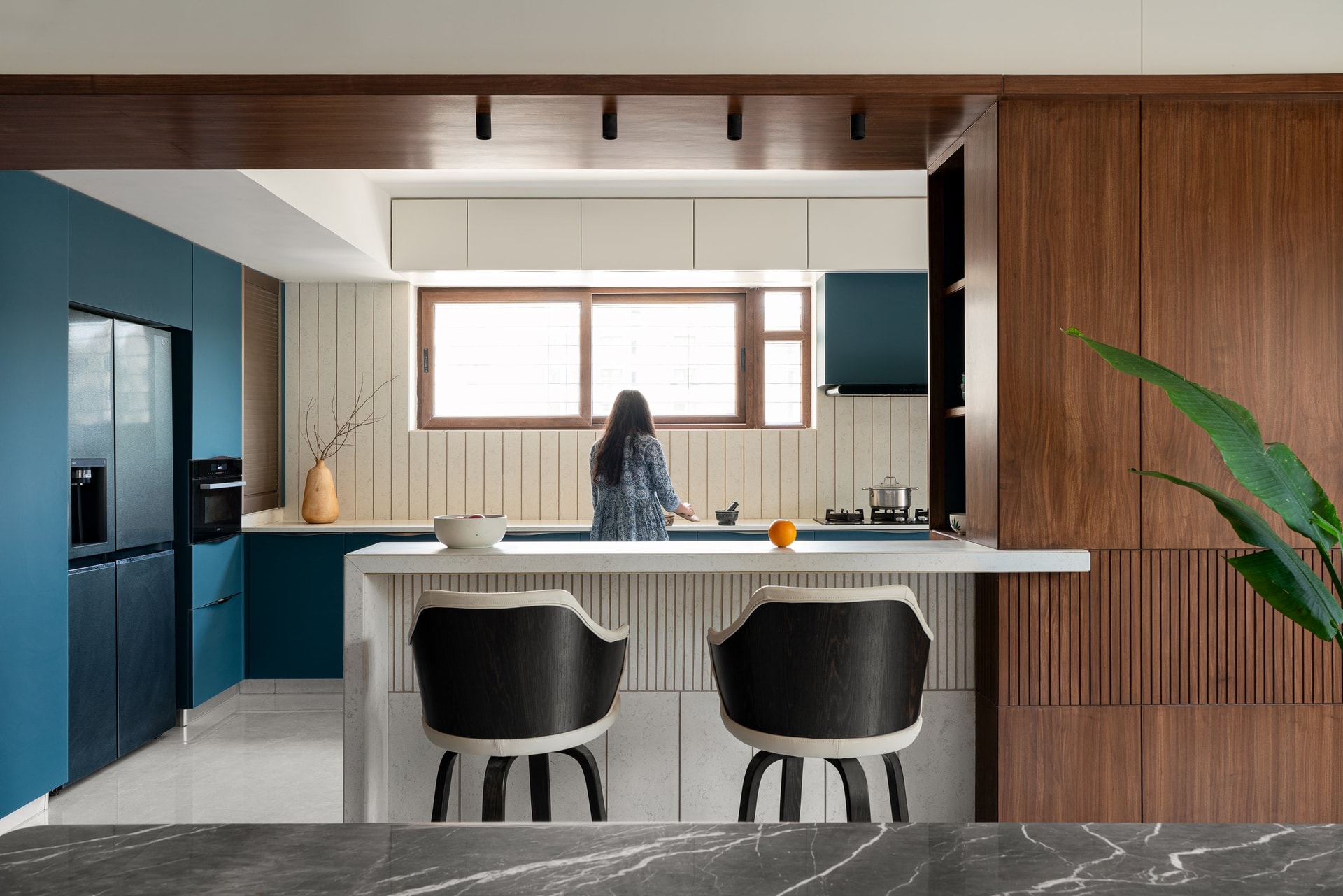 The kitchen opens to the dining room through a stone breakfast counter, with deep teal cabinetry against a fluted cream backsplash