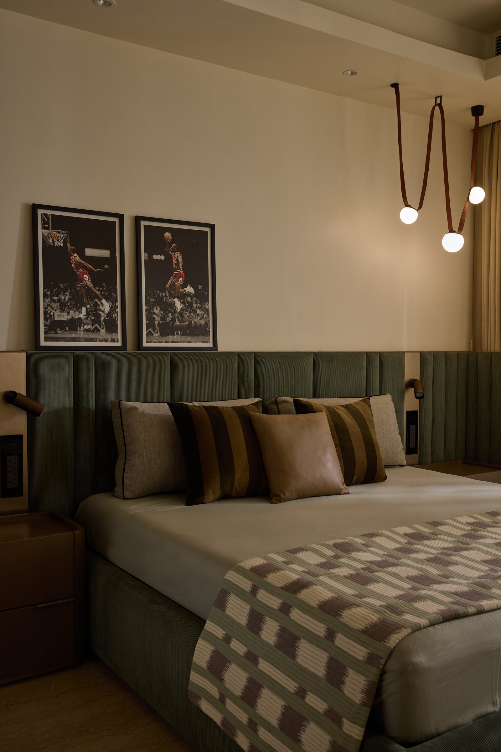 The second bedroom: framed basketball prints above an olive velvet headboard, with spherical pendants on looped leather straps