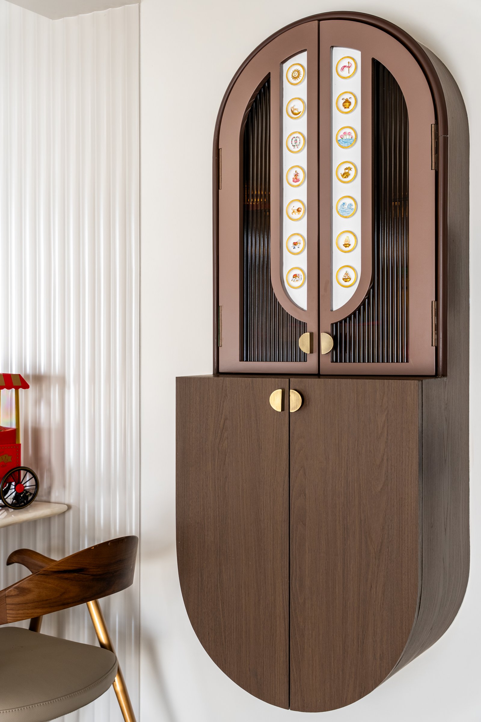 A wall-mounted bar cabinet just off the dining area, its medallion-decorated reeded glass doors operating as personal storytelling embedded in cabinetry