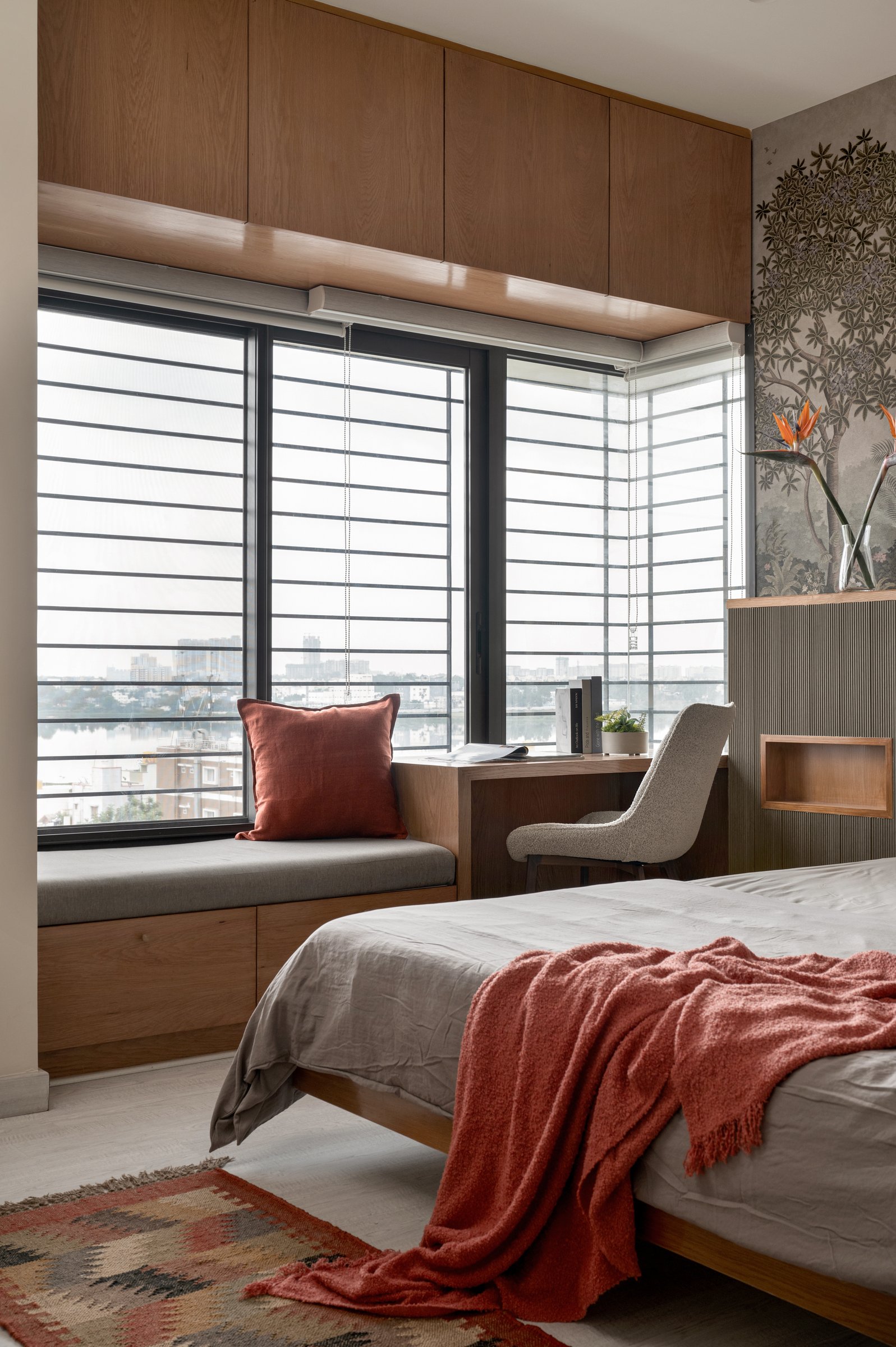 The window seat extends the writing desk into a generous perch, framing the Bengaluru skyline as part of the room's composition