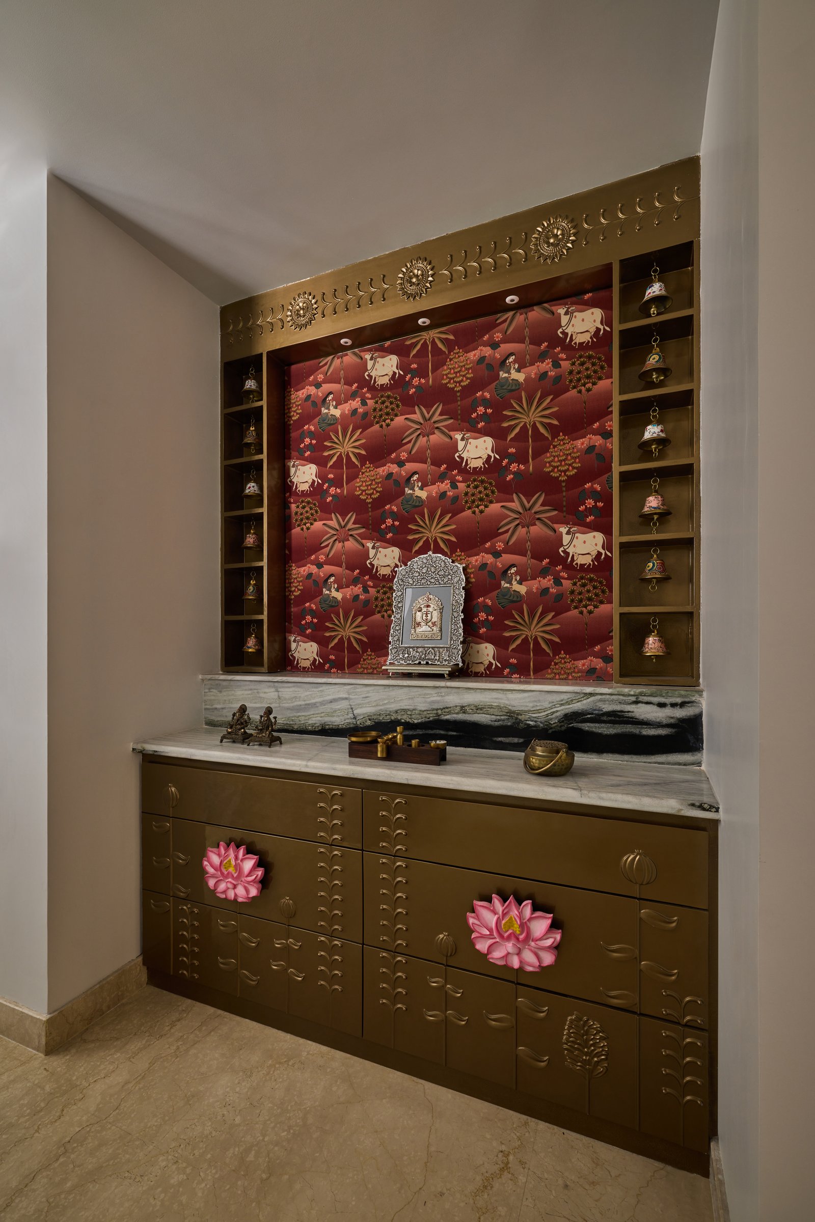 The pooja niche: a printed Pichwai-style panel in deep red, framed by brass-clad shelving