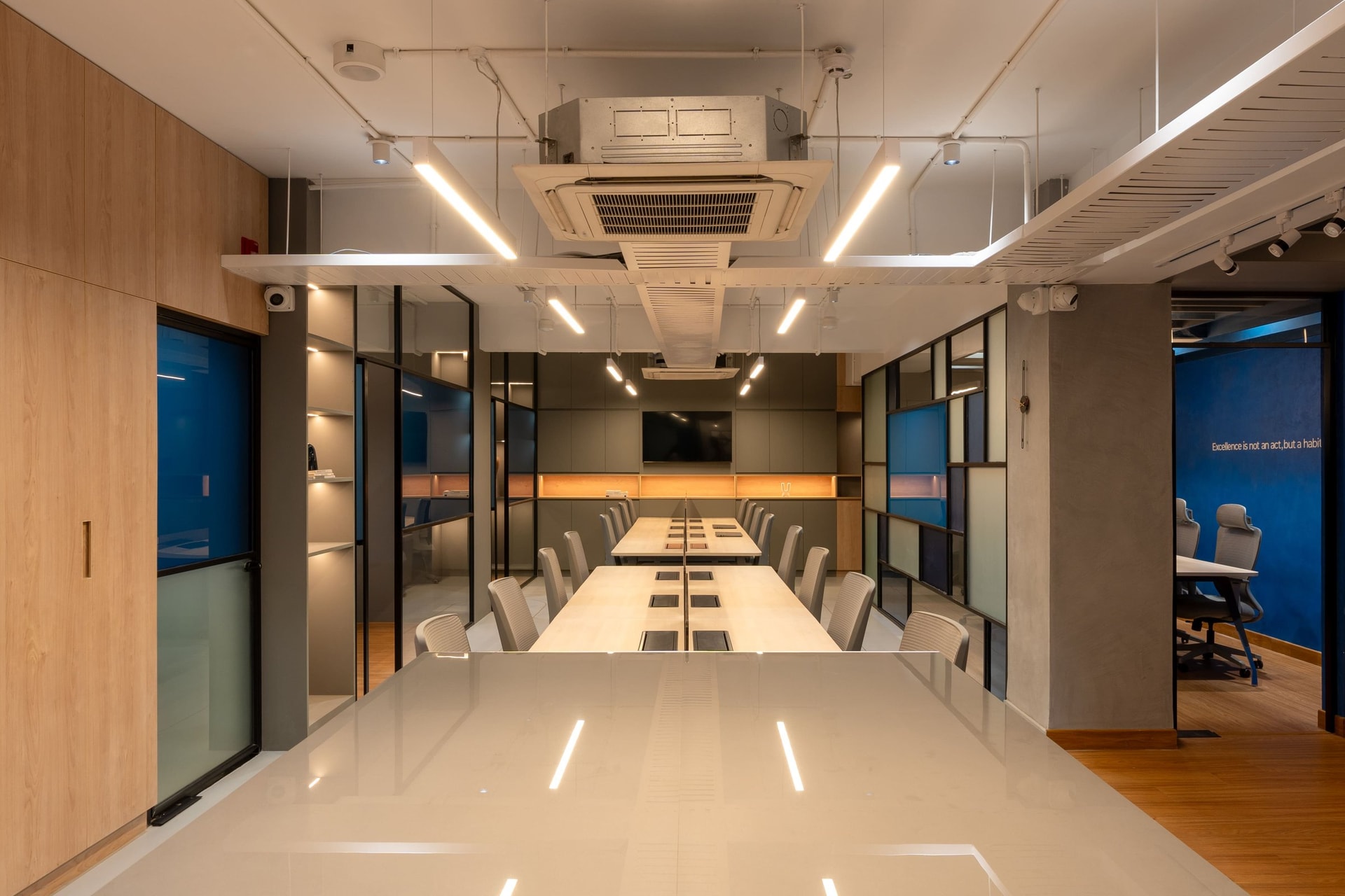 The central spine: gridded glass partitions in clear, frosted, and tinted panes carry daylight from perimeter cabins through the floor plate