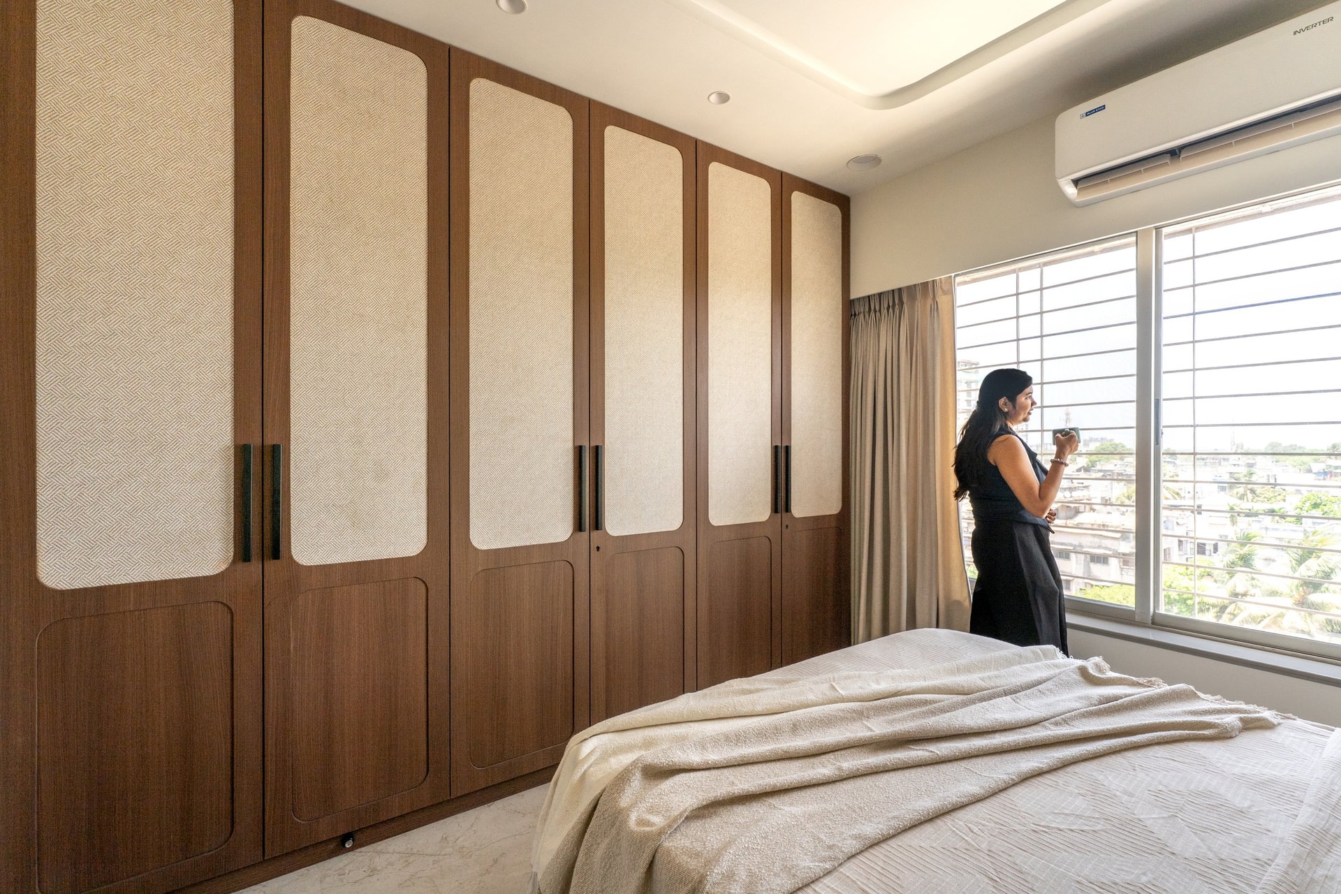 A second bedroom takes a more restrained turn: walnut wardrobes with cane-textured inserts, a wide window admitting city light