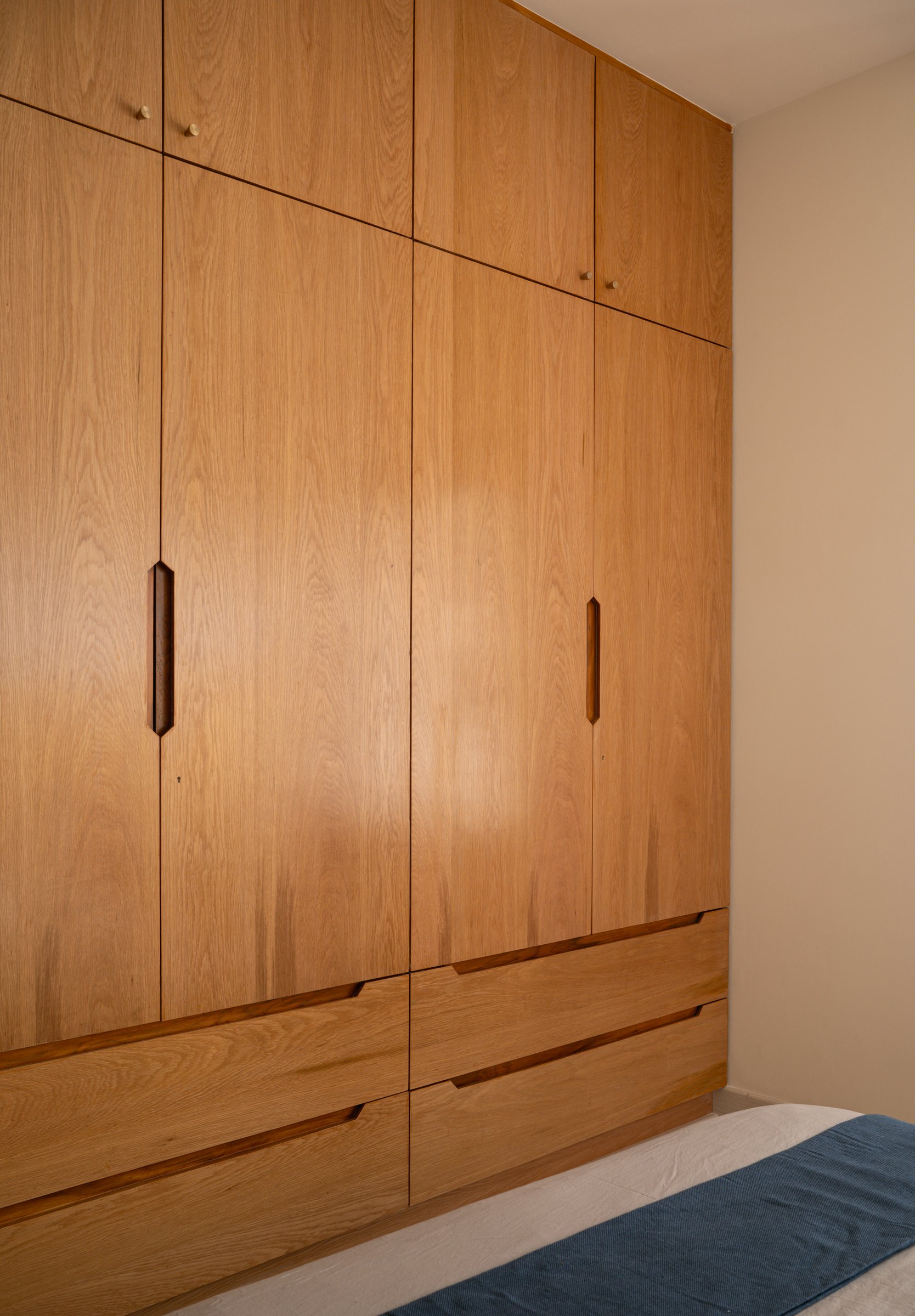 The master wardrobe spans a full wall in clean wood-grain panels, its capacity absorbed almost invisibly into the architecture